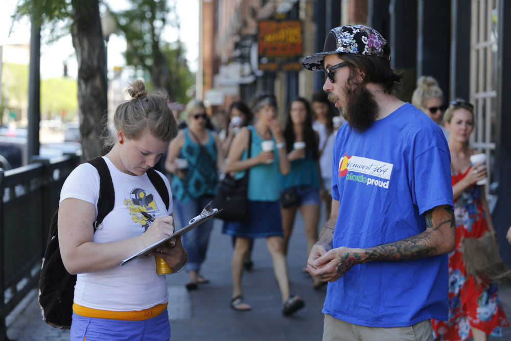 In this June 11 photo, Damian Riniker, right, a marijuana reform advocate with the group NORML, stands by while a passerby signs a petition to get a pot club initiative on the ballot in the next election, in Denver.