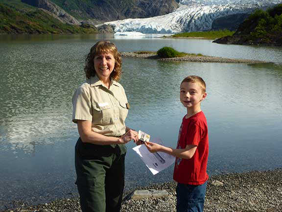 Rosary Lombardo hands out an Every Kid in a Park pass to a Juneau fourth grader in front of the Mendenhall Glacier.