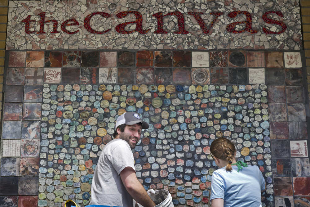 Artistic Coordinater Brandon Howard and summer intern Dara DeGrave add the final grout to a tile mural in front of The Canvas Gallery & Studio on June 29. Canvas artist Susy Martin made nearly 2,000 clay faces. Larger square tiles made by community members during a fundraiser form the border of the mural, and Marianne Manning made the glass mosaic top.
