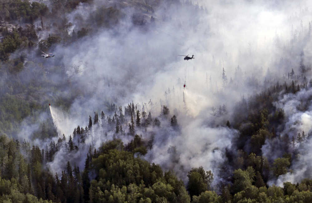 In this Wednesday, July 20, 2016 photo provided by the U.S. Army National Guard, an Alaska Army National Guard UH-60 Black Hawk helicopter and a State of Alaska Division of Forestry helicopter dump several thousand of gallons of water onto the McHugh Creek fire near Anchorage, Alaska. The wildfire threatening homes just south of Alaska's largest city was likely started by people, fire officials said Wednesday. The cause is under investigation, and officials said the area is heavily used for recreation.