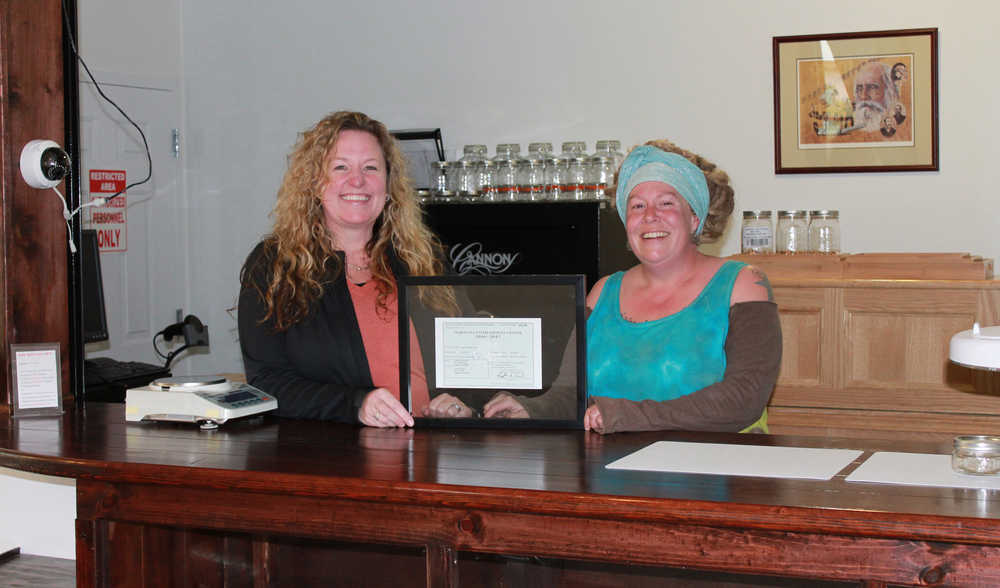Tara Bass, left, and budtender Reba Radey, right, hold the new retail marijuana license awarded Skagway's The Remedy Shoppe on Oct. 4, 2016. The store is the first in Alaska to receive its retail license.