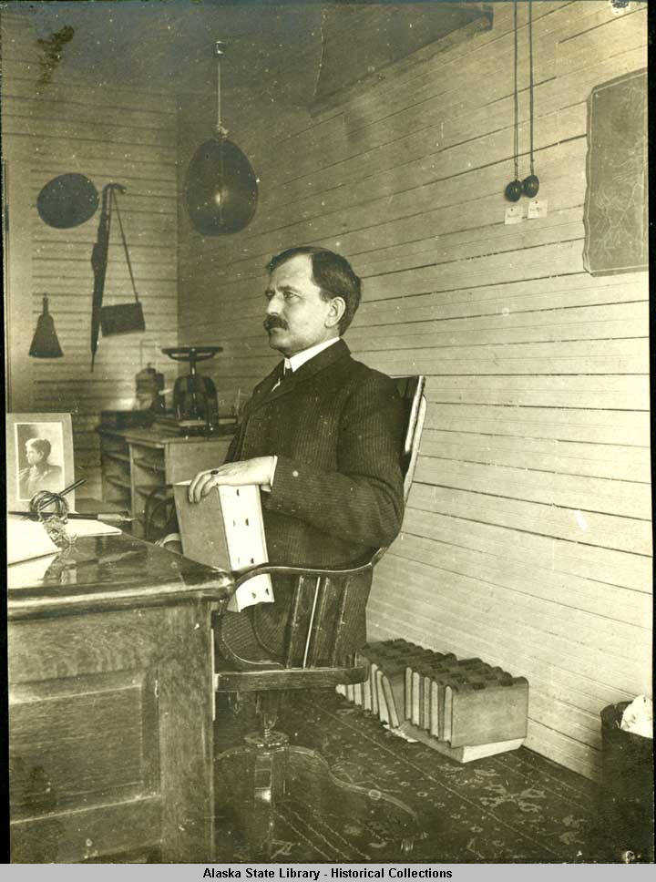 James Wickersham seated at his desk with law books.