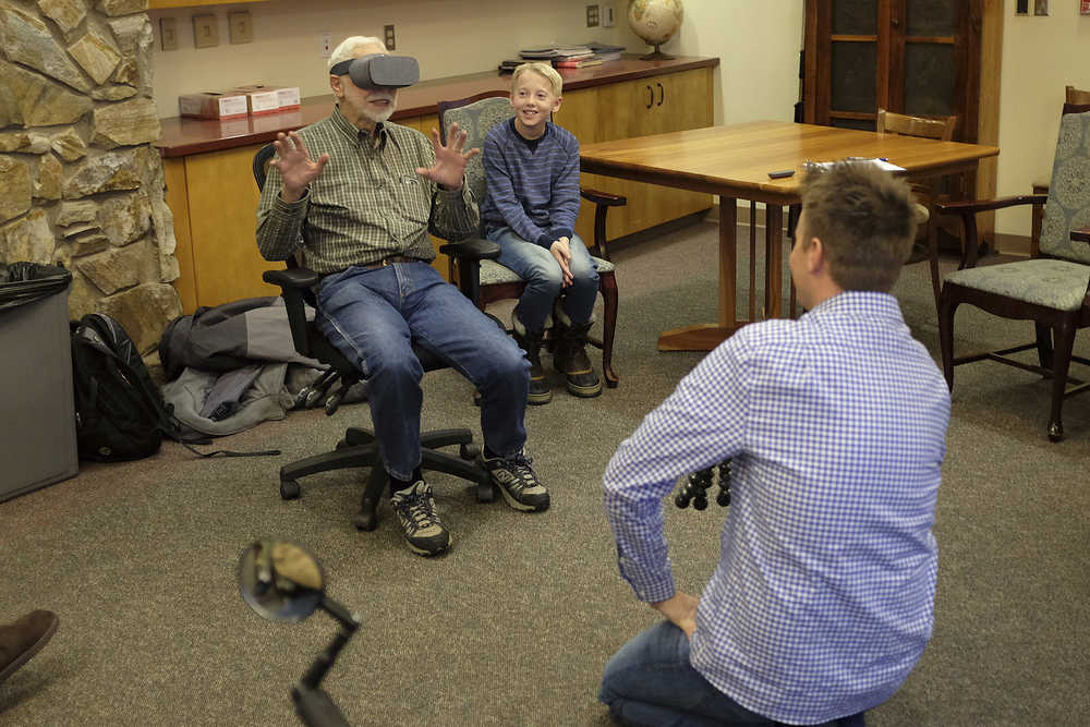 ADVANCE FOR SATURDAY DEC. 24, 2016 AND THEREAFTER - In this Dec. 13, 2016 photo, Pioneers Home resident Joe Nistler, 90, reacts to a virtual reality video of a herd of elephants walking while Lincoln Markham, right, watches in Fairbanks, Alaska. Lincoln Markham and Dan Markham are the father-son duo behind the extremely popular What's Inside YouTube channel. (Matt Buxton/Fairbanks Daily News-Miner via AP)