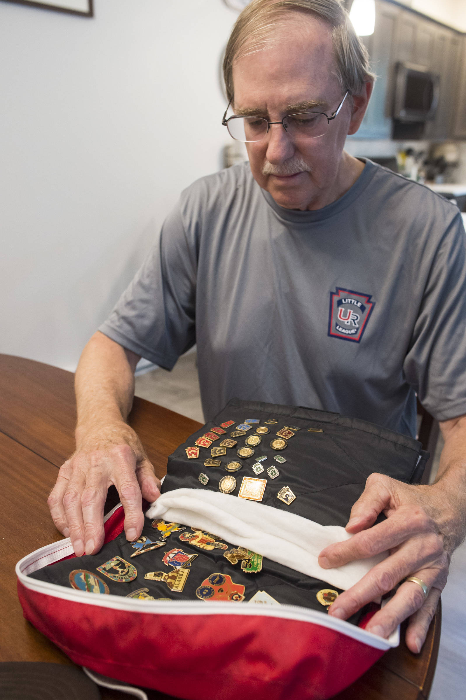 Tom Karpstein, 70, show a portion of his collection of baseball tournament pins as he talks Thursday, August 2, 2018, about his long baseball umpiring role in Juneau. (Michael Penn | Juneau Empire)