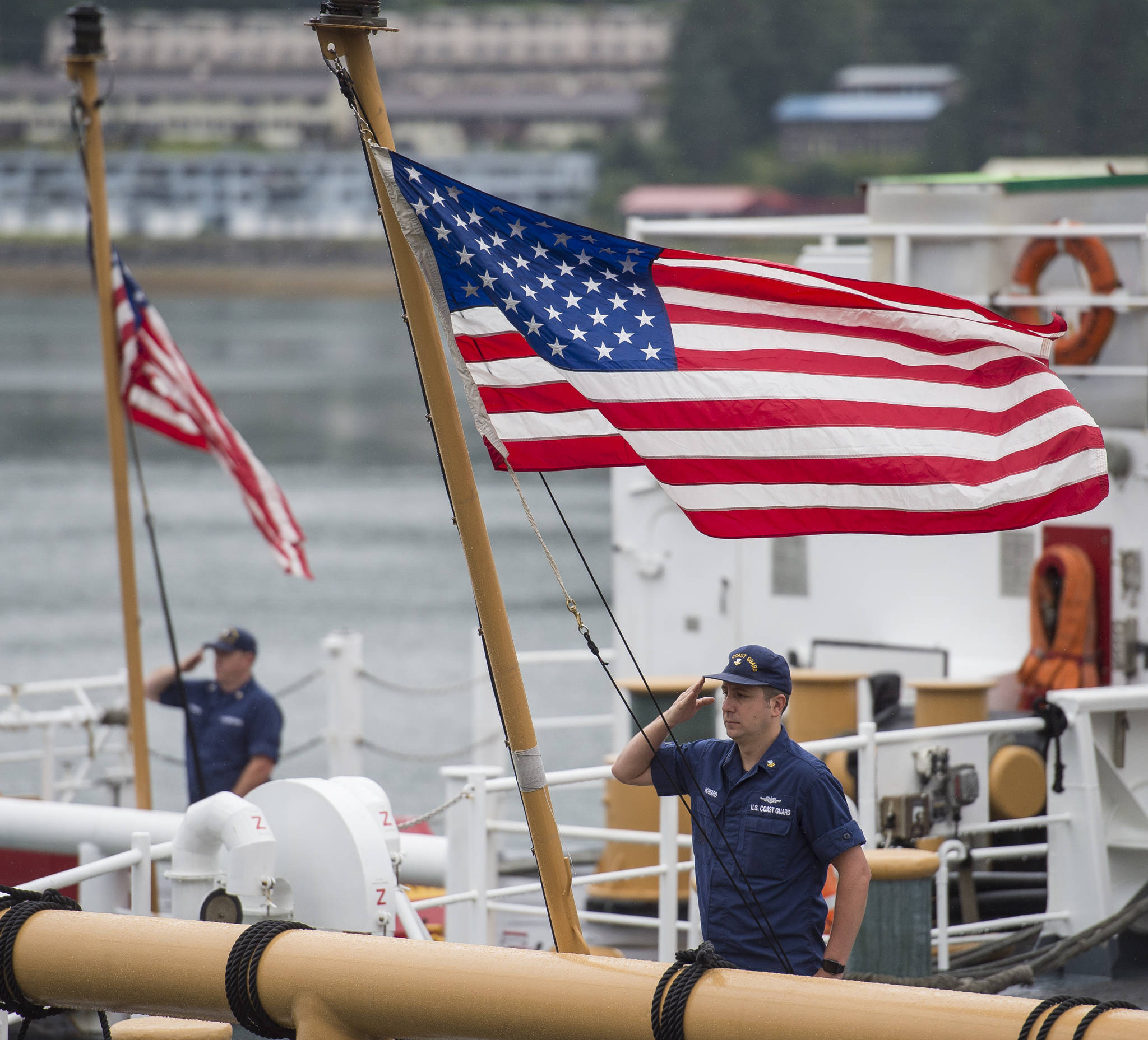 Flags are raised on U.S. Coast Guard buoy tenders for reveille before the start of the Buoy Tender Olympics at Station Juneau on Wednesday, Aug. 22, 2018. (Michael Penn | Juneau Empire)