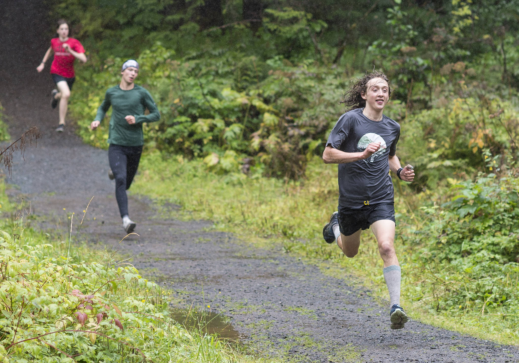 Senior Arne Ellefson-Carnes, right, leads JDHS graduate Zack Bursell, center, and sophomore Finn Morley down a hill during Juneau-Douglas High School cross country practice at Sandy Beach at the Treadwell Historic Mining Area on Tuesday. (Michael Penn | Juneau Empire)