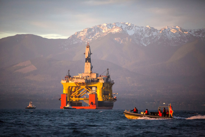 In this April 2015 file photo, with the Olympic Mountains in the background, a small boat crosses in front of an oil drilling rig as it arrives in Port Angeles, Washington, aboard a transport ship after traveling across the Pacific. Royal Dutch Shell PLC confirmed Tuesday it will relinquish all but one of its federal offshore leases in Alaska's Chukchi Sea.