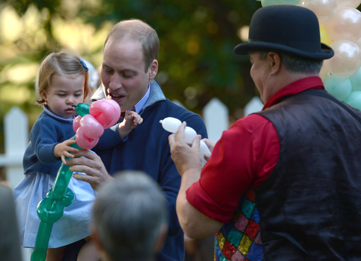Britain's Prince William, the Duke of Cambridge, holds Princess Charlotte, as she is given a balloon animal during a children's tea party at Government House in Victoria, British Columbia, Thursday