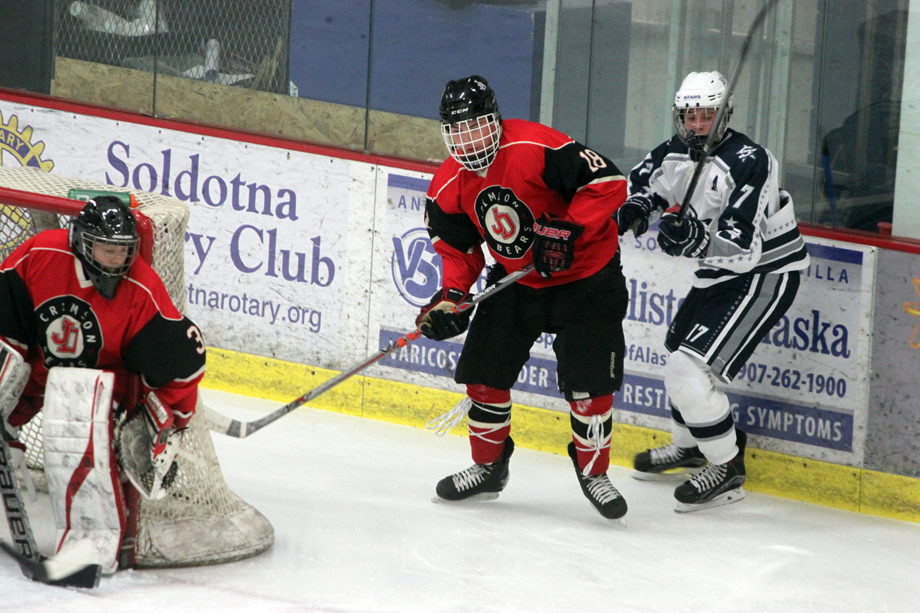 Juneau-Douglas defender Niko Hebert chases the puck behind goalie Kyle Farley-Robinson, Thursday at the Soldotna Regional Sports Complex.
