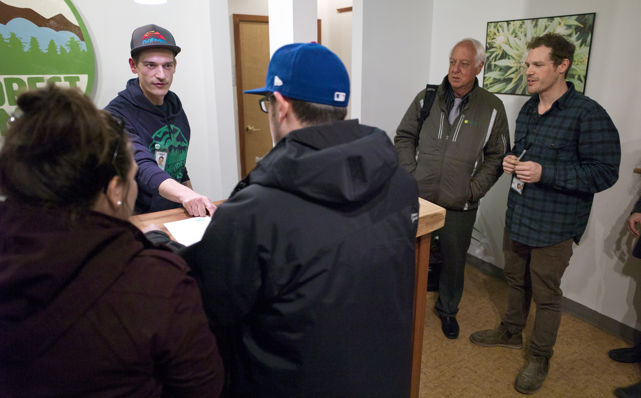 In this file photo, Juneau Mayor Ken Koelsch, center, stands and watches the first marijuana sales in the capital city with Giono Barrett, right, as James Barrett helps customers during a invitation opening of Rainforest Farms store on Nov. 23, 2016. (Michael Penn | Juneau Empire File)