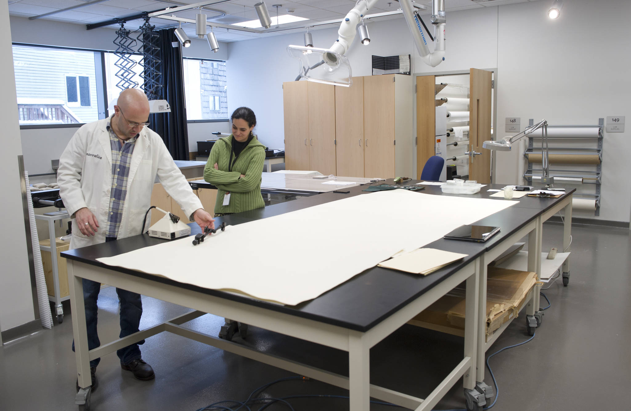 Ellen Carrlee, objects conservator at the Alaska State Museum, watches Seth Irwin, a paper conservator from Boston, working at the Alaska State Museum on Sesquicentennial documents that will go on display later this year. (Michael Penn | Juneau Empire)