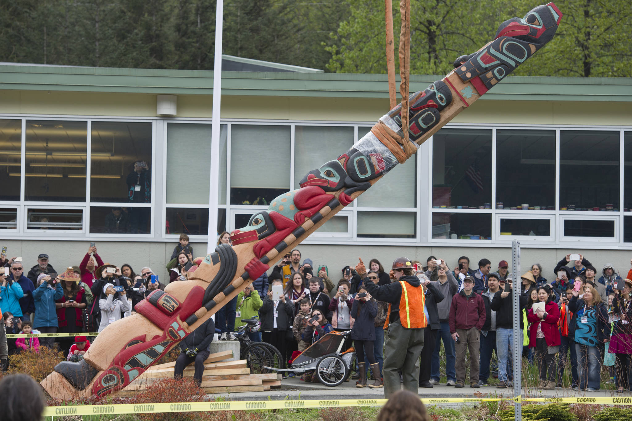 Juneau residents watch as a raven totem pole is lifted into place by Trucano Constructuion at Gastineau Elementary School on Saturday, May 13, 2017. The 26-foot pole, paid for by the Goldbelt Heritage Foundation, honors the Gaanaxteid&
