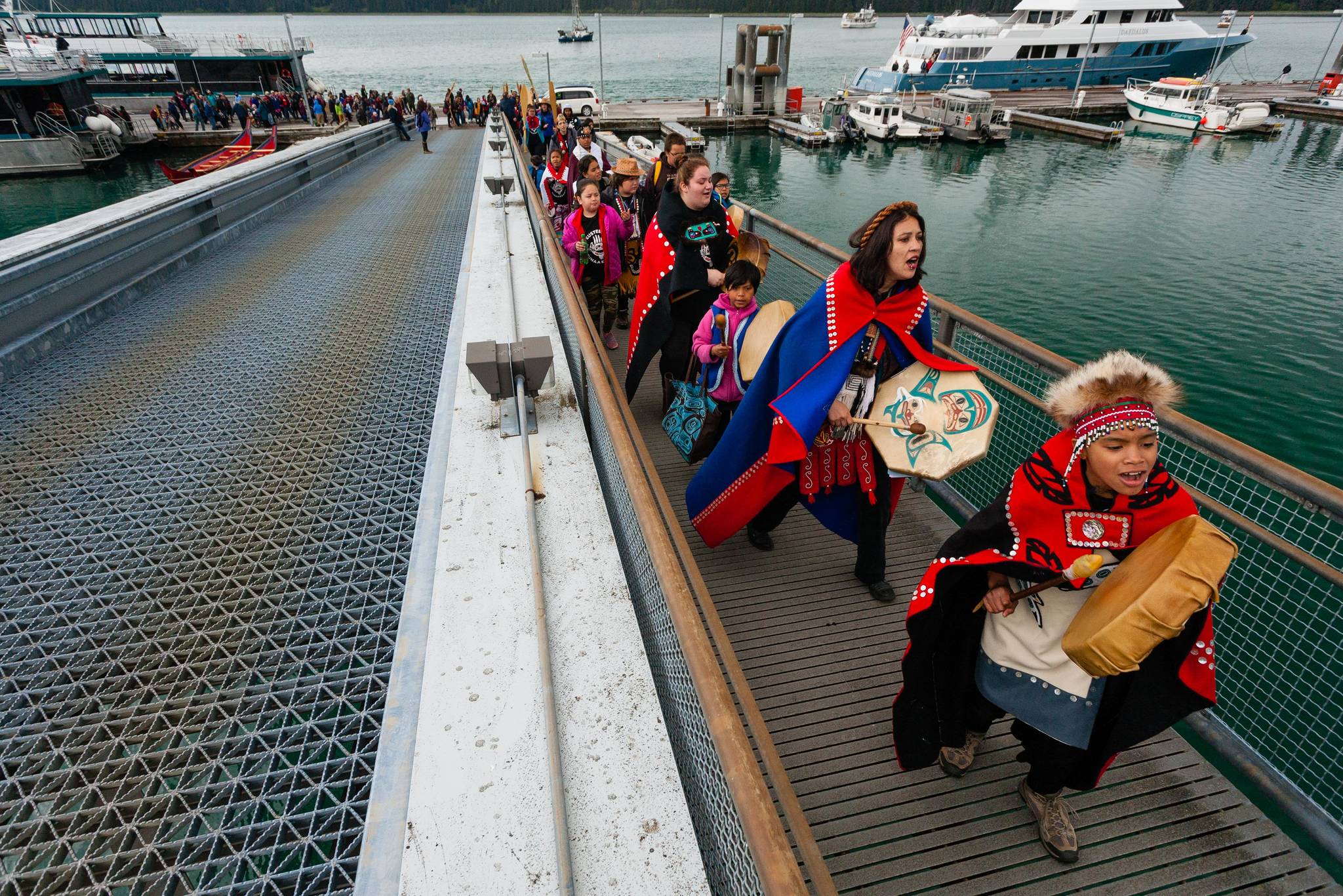 Hoonah City School students drum their way up the dock to greet the waiting totem poles. (Mary Beth Moss | For the Capital City Weekly)