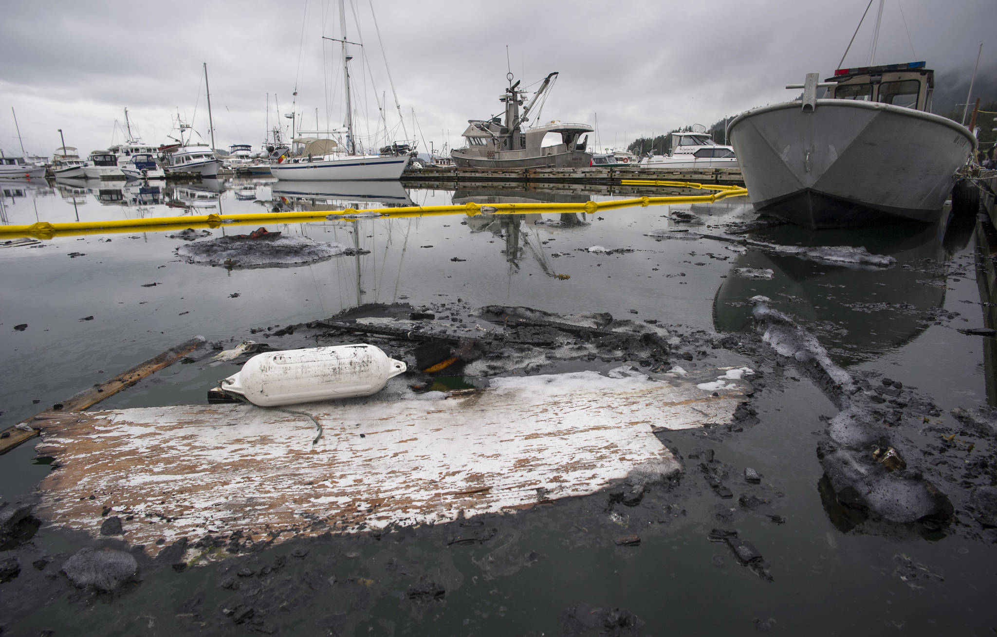 The charred remains, debris and fuel float in the Don D. Statter Memorial Boat Harbor in Auke Bay on Tuesday, June 27, 2017. One boat occupant was taken to the hospital for smoke inhalation after a boat in Auke Bay caught fire and sank Tuesday morning. (Michael Penn | Juneau Empire)