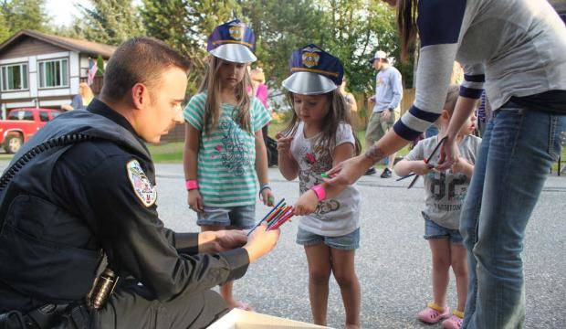 Juneau Police Department Officer Ben Beck hands out pencils and paper police hats to neighborhood kids in the Mendenhall Valley during National Night Out in this 2015 archive photo. (Emily Russo Miller | Juneau Empire File)