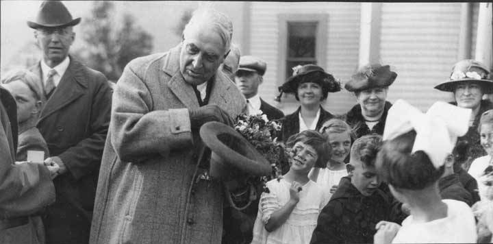 President Harding holds flowers as he greets children in Skagway, 1923. From the Marguerite Bone Wilcox collection, identifier ASL-P70-20. Image courtesy of the Alaska State Library Historical Collections.