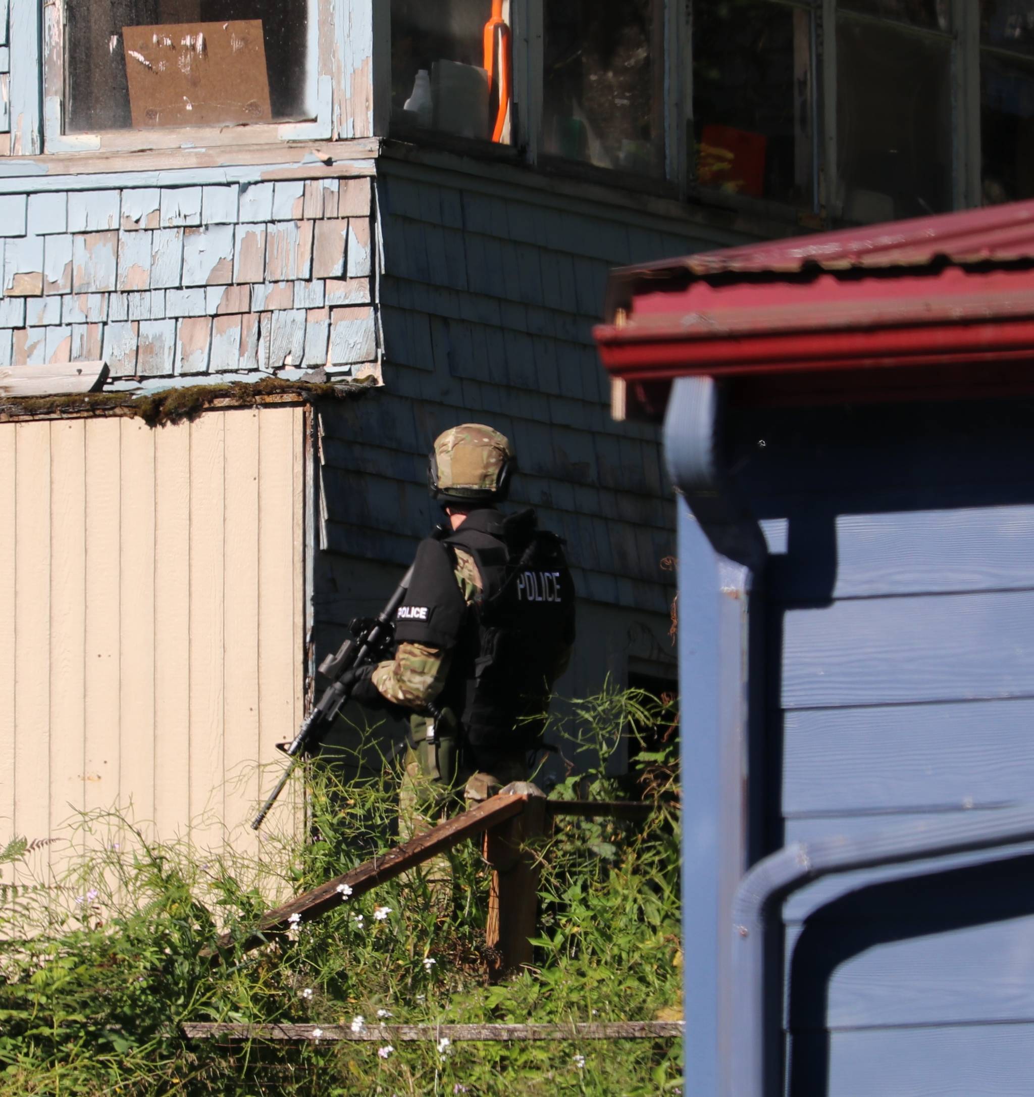 A Juneau Police Department officer stops while circling the house and peering in the windows to see who is inside, while the warrant search was under way at 423 Fourth St. on Friday afternoon. (Photo courtesy of Matt Gruening)