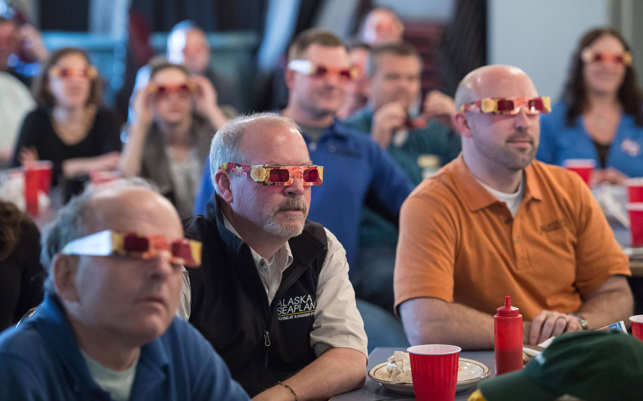 Attendees of the Juneau Chamber of Commerce luncheon don “rose-colored glasses” to view economic data presented by Brian Holst, executive director of the Juneau Economic Development Council at the Moose Lodge on Thursday, Sept. 28, 2017. (Michael Penn | Juneau Empire)