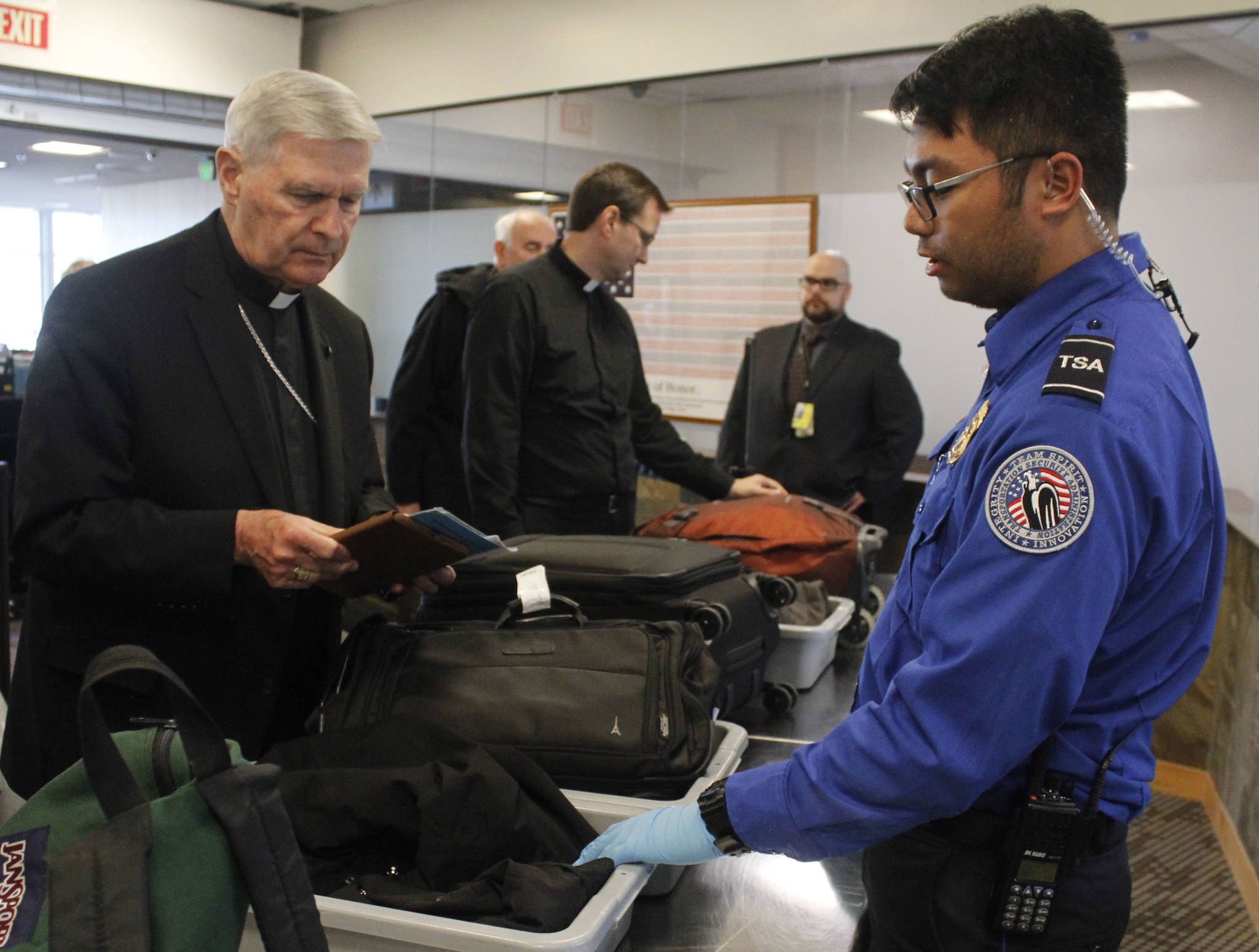 Transportation Security Officer Renier Cava gives instructions to Father Roger Schwietz on Wednesday, Oct. 11 at the Juneau International Airport. A new policy from the Transportation Security Administration requires passengers to remove all electronic items larger than their cell phones and put them through the scanner. (Alex McCarthy | Juneau Empire)