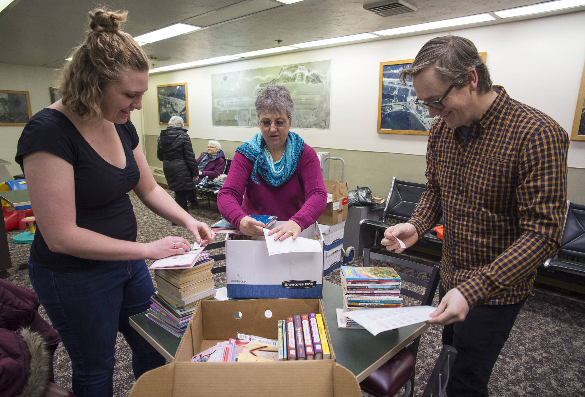 Hannah Weed, of the Association for the Education of Young Children, left, Louise Miller, of the Friends of the Juneau Public Libraries, center, and Juneau Public Librarian Jonas Lamb apply stickers to books for a new bookshelf for children at the Juneau International Airport on Wednesday, Nov. 15, 2017. A partnership between United Way, AEYC, Friends of The Juneau Public Libraries, Alaska Airlines and the Juneau Airport, the “Read on the Fly” program will offer free books to children to take as they travel to or from Juneau.