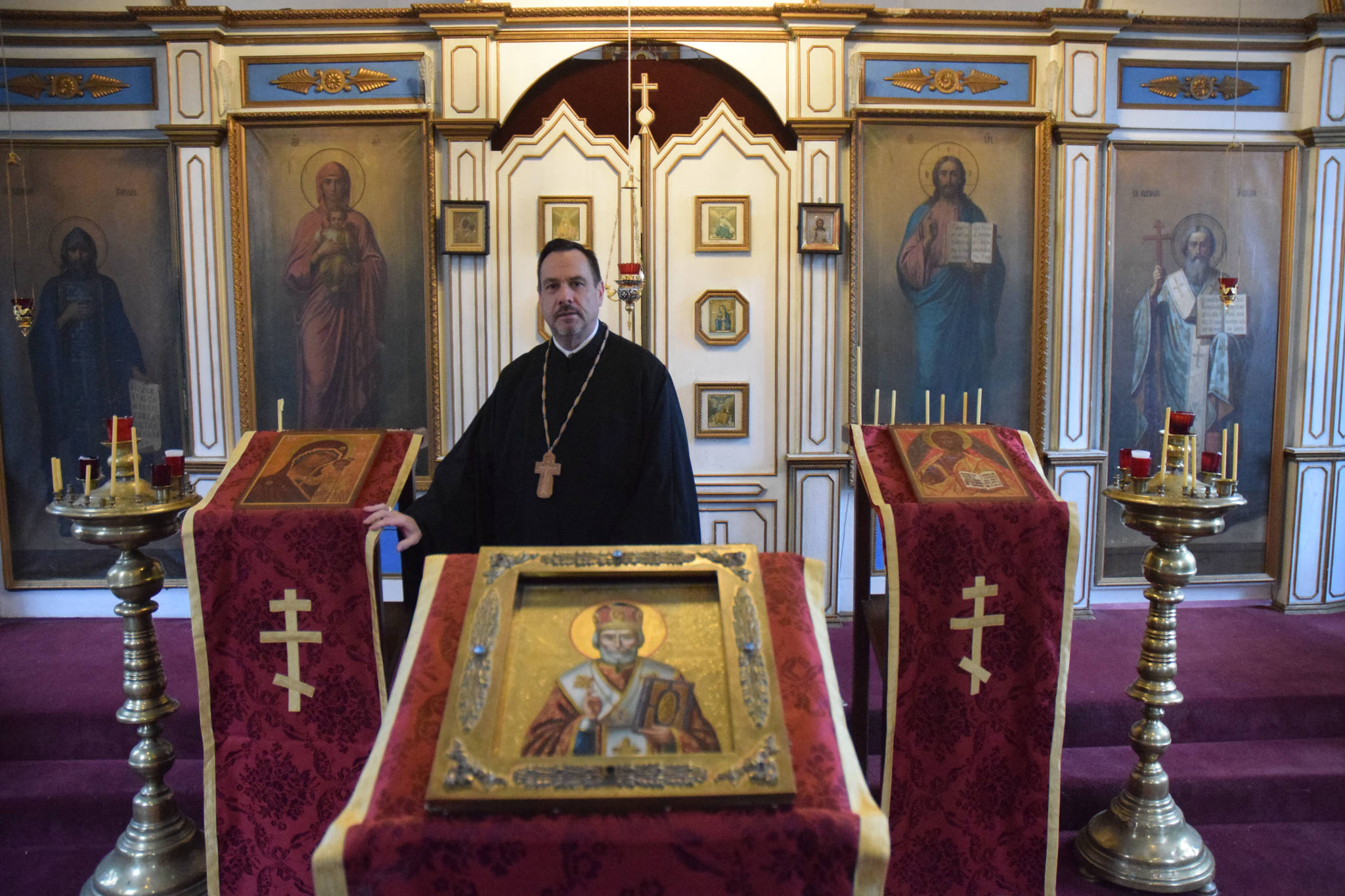 Father Steven McGuigan poses in front of the icon of St. Nicholas at St. Nicholas Russian Orthodox Church on Friday. (Kevin Gullufsen | Juneau Empire)