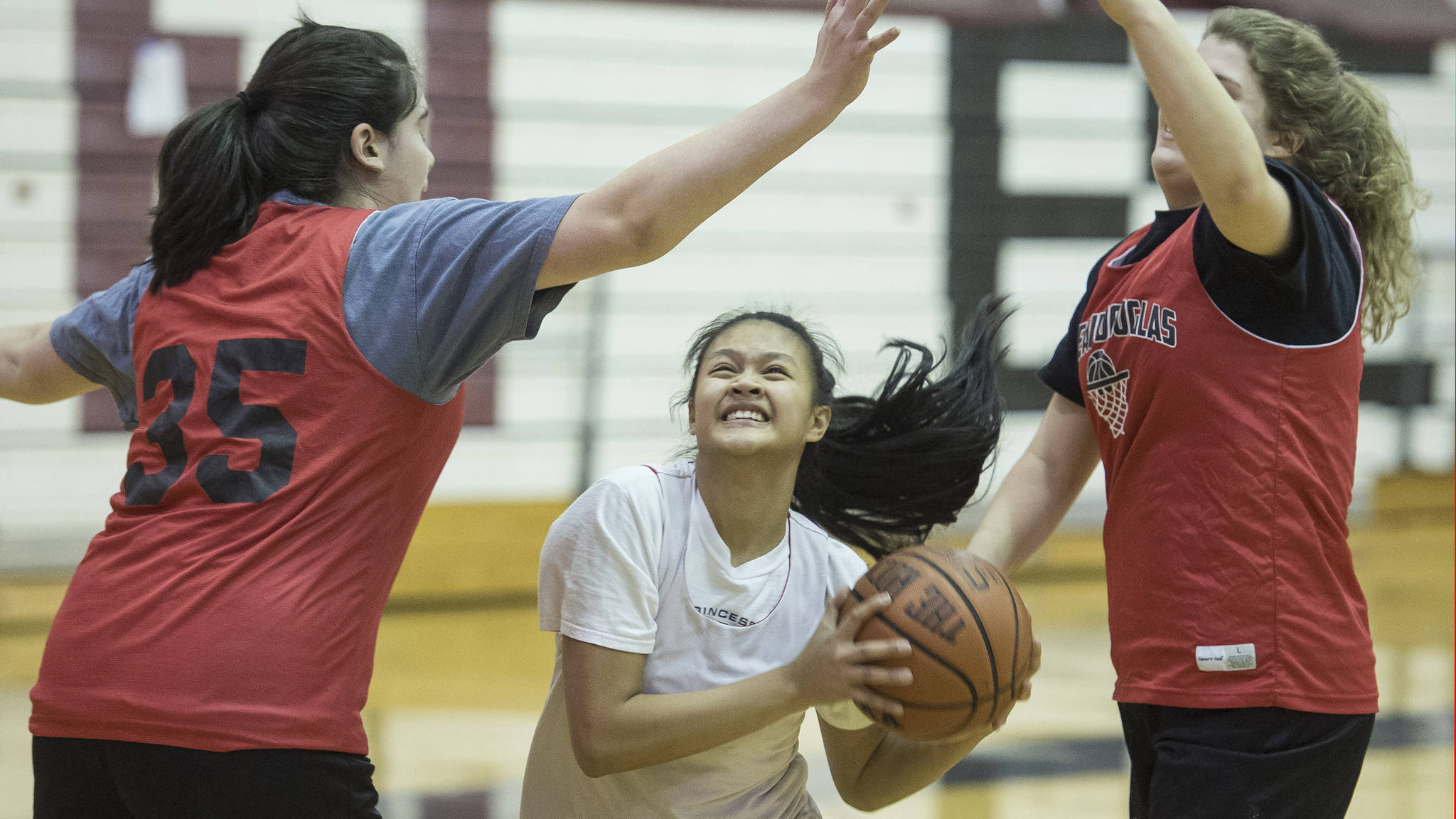 Alyxn Bohulano drives to the basket between teammates Chloe McAdams, left, and Skylar Hickok at Juneau-Douglas High School girls basketball practice on Thursday, Dec. 7, 2017.
