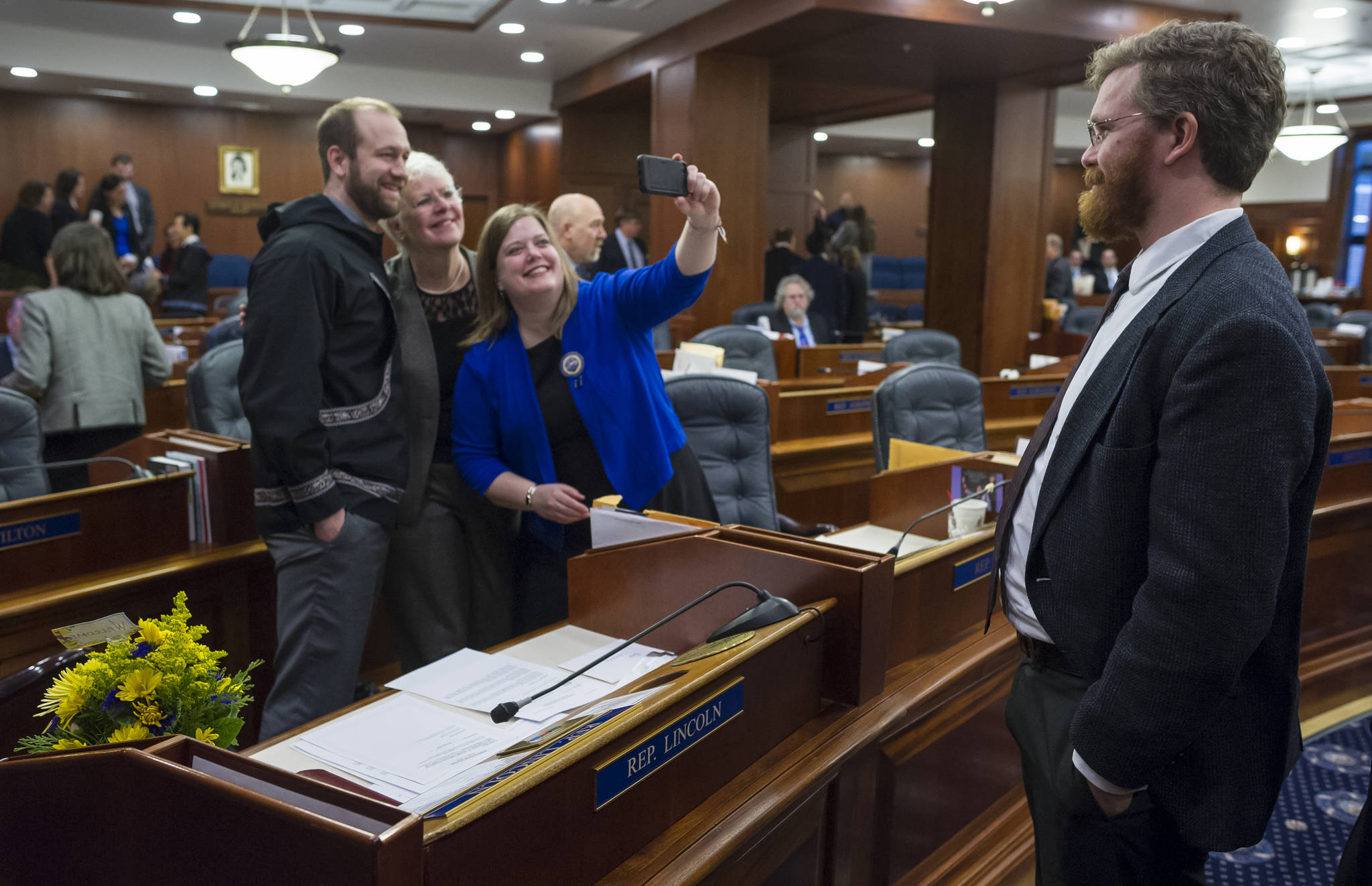 Rep. John Lincoln, D-Kotzebue, left, has his picture taken with Rep. Louise Stutes, R-Kodiak, by Rep. Geran Tarr, D-Anchorage, as Rep. Justin Parish, D-Juneau, watches in the House chambers on Wednesday, Jan. 31, 2018. (Michael Penn | Juneau Empire)