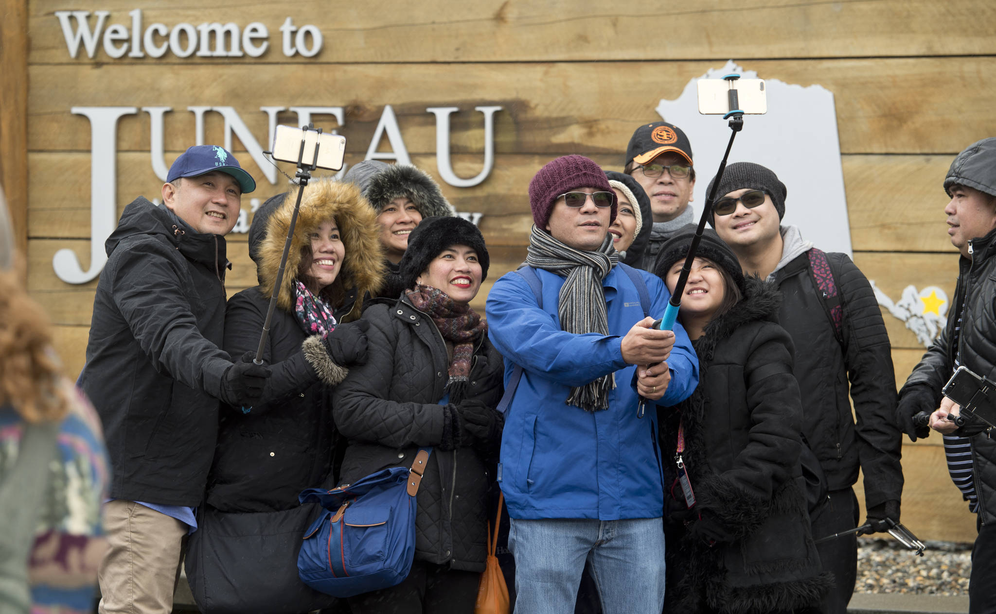 In this May 1, 2017 photo, tourists line up with their selfie sticks in front of the “Welcome to Juneau” sign after arriving by the first cruise ships of the season. (Michael Penn | Juneau Empire File)