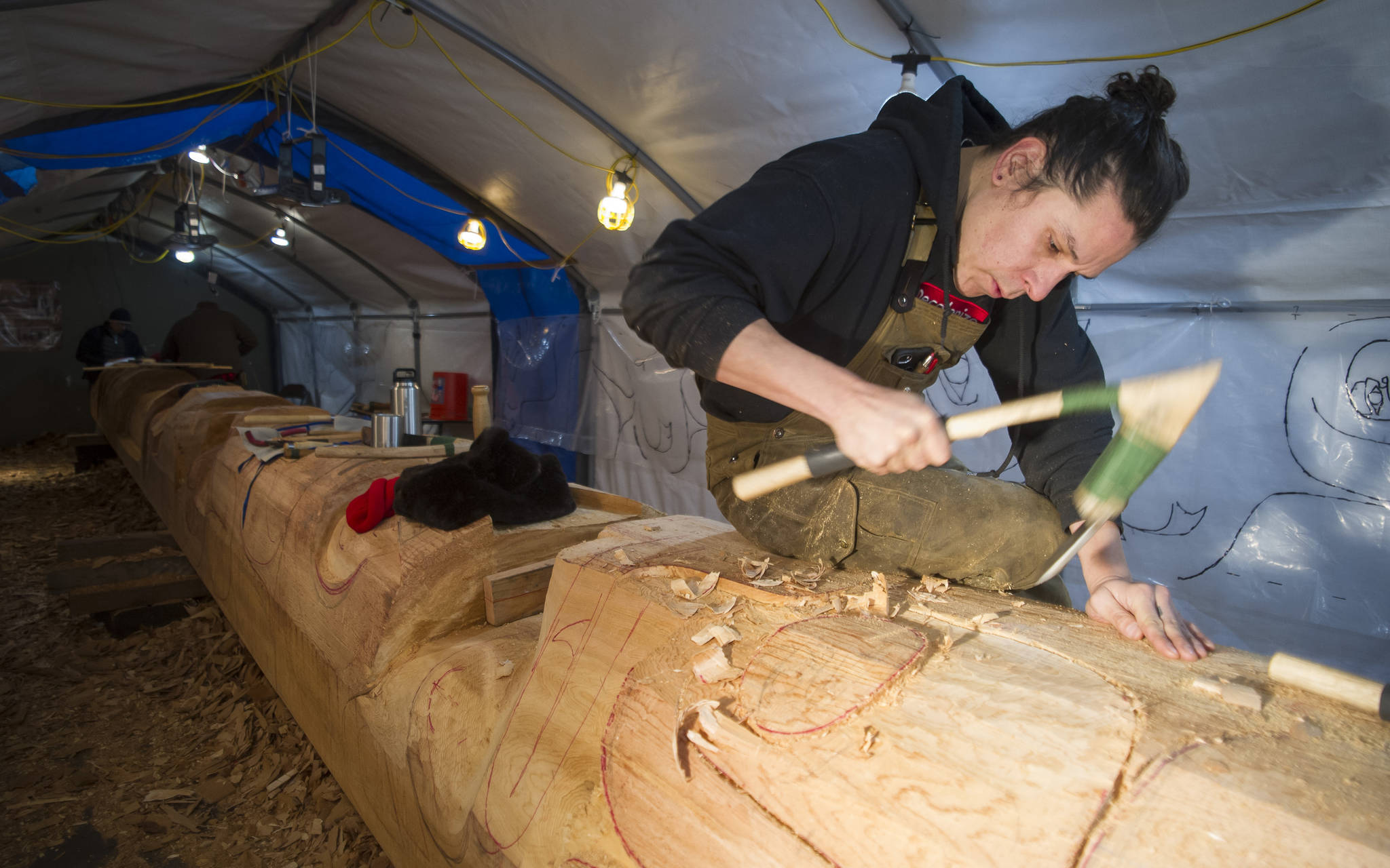In this Dec. 5, 2017 photo, lead carver Nicholas Galanin works on the Wolf Totem Pole at Harborview Elementary School. (Michael Penn | Juneau Empire File)
