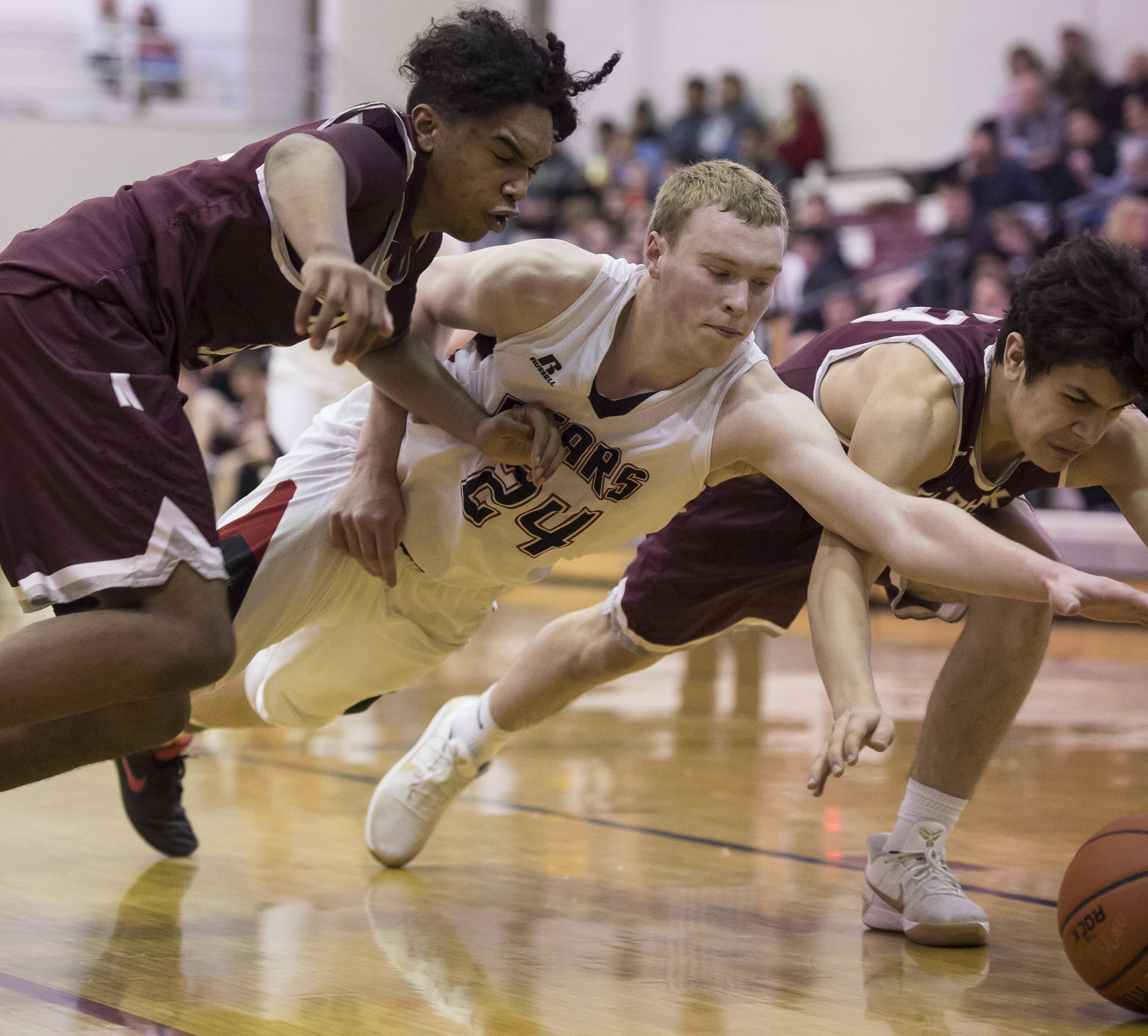 Juneau-Douglas’ Erik Kelly, center, dives for a ball against Ketchikan’s Chris Lee, left, and James Nordlund at JDHS on Wednesday, Feb. 21, 2018. JDHS won 59-41.