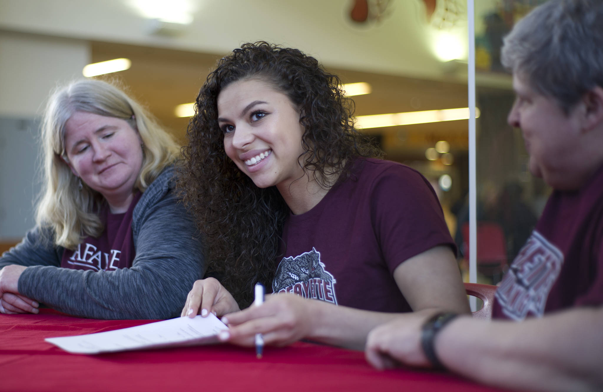 Juneau-Douglas High School senior Andyn Mulgrew-Truitt signs her national letter of intent to swim at Lafayette College in Easton, Pennsylvania, next to parents Loveann Truitt, left, and Laura Mulgrew on Wednesday at the JDHS commons. (Nolin Ainsworth | Juneau Empire)