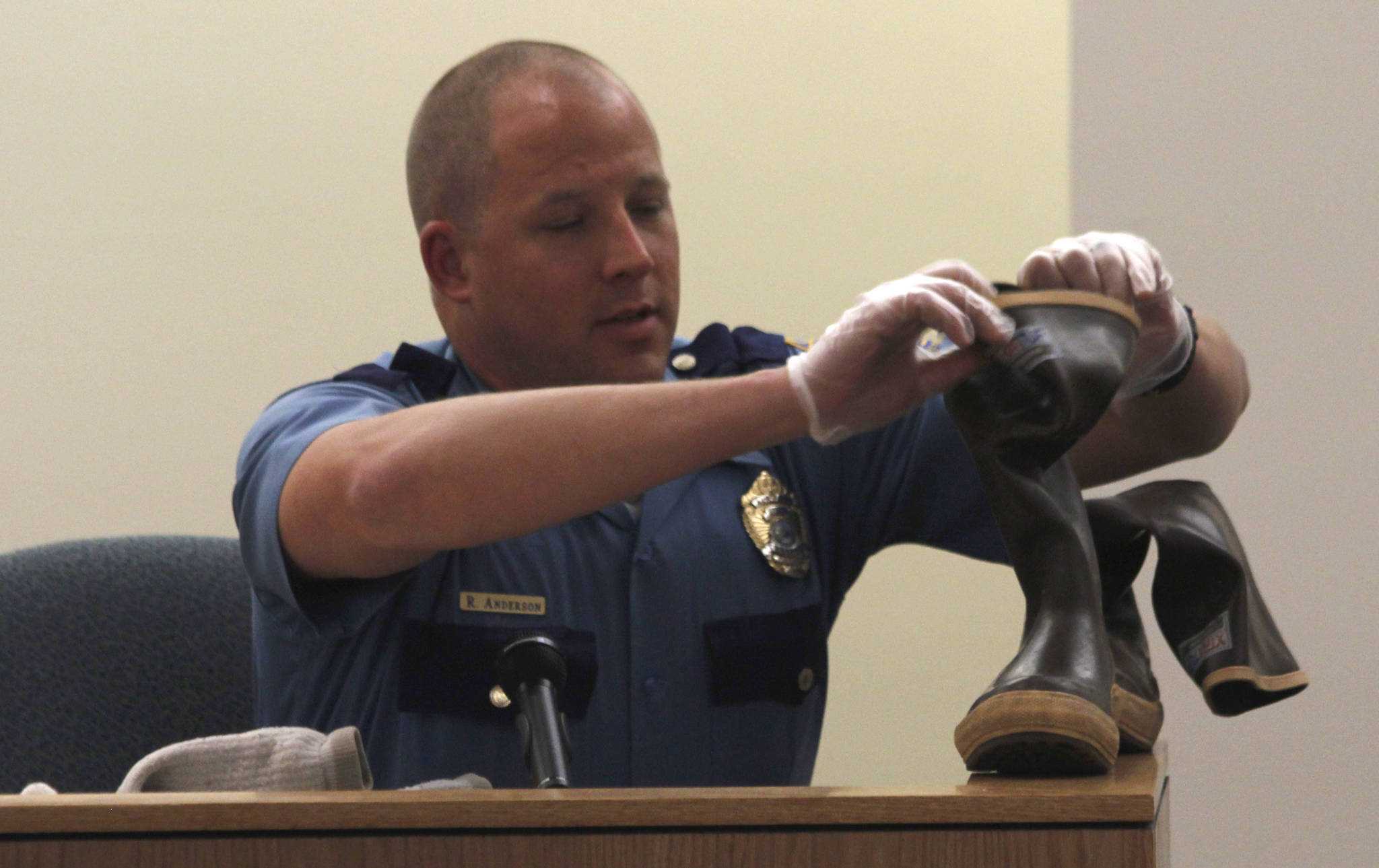 Alaska State Trooper Ryan Anderson illustrates how Duilio Antonio “Tony” Rosales’ boots were arranged when Anderson found Rosales deceased at an Excursion Inlet cabin in 2016. Anderson is a witness in the trial of Mark De Simone, who is accused of shooting and killing Rosales. (Alex McCarthy | Juneau Empire)
