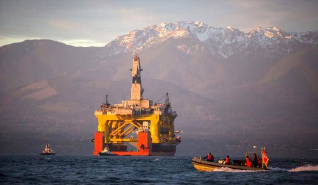 In this April 2015 file photo, with the Olympic Mountains in the background, a small boat crosses in front of an oil drilling rig as it arrives in Port Angeles, Washington, aboard a transport ship after traveling across the Pacific. (AP File Photo)