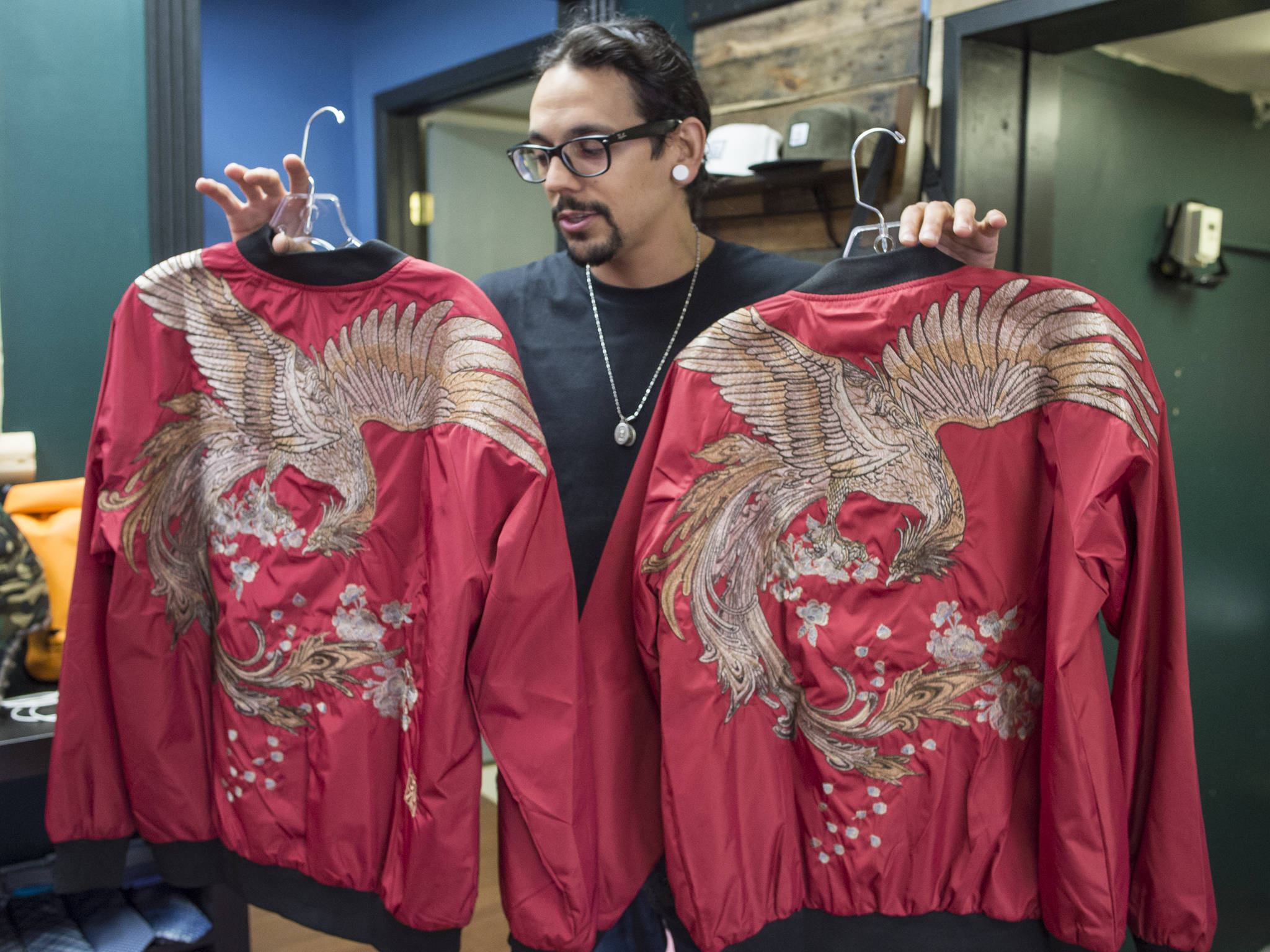 Gabriel Rivera, of 4th Coast Outfitters, holds up a pair of embroidered phoenix bomber jackets on Wednesday, May 16, 2018, he thinks will be worn in this weekend’s Flappers Fashion show. (Michael Penn | Juneau Empire)