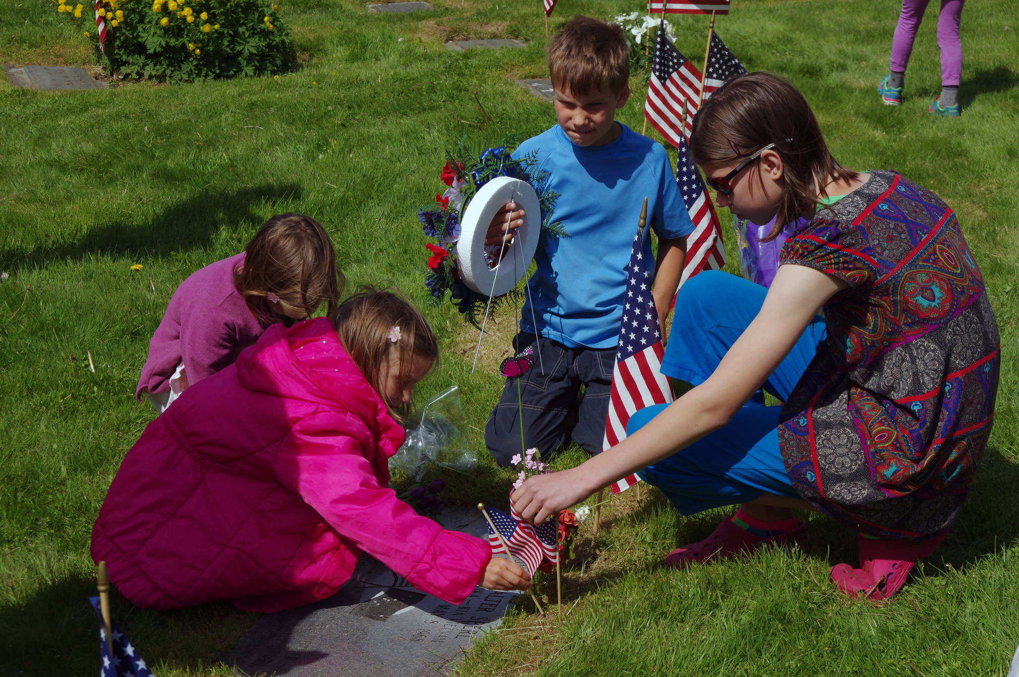 Children arrange flowers and a flag around their great-uncle’s grave following a Memorial Day service at Evergreen Cemetery on Memorial Day 2014. (Matt Woolbright | Juneau Empire File)