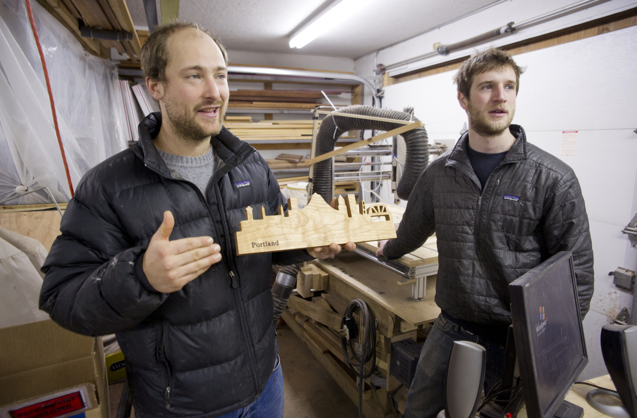Local woodworkers Max Stanley and Chris Hinkley, of Latitude Woodwares, in their Auke Bay shop on Thursday. The craftsmen, known for wood topographical maps of Southeast, launched a crowdsourcing campaign this week in an attempt to expand their business to national markets. The pair have developed what they call “skyline hangs” — magnetic knife hangers shaped into cityscapes — they hope will sell big in major metropolitan areas. (Michael Penn | Juneau Empire)