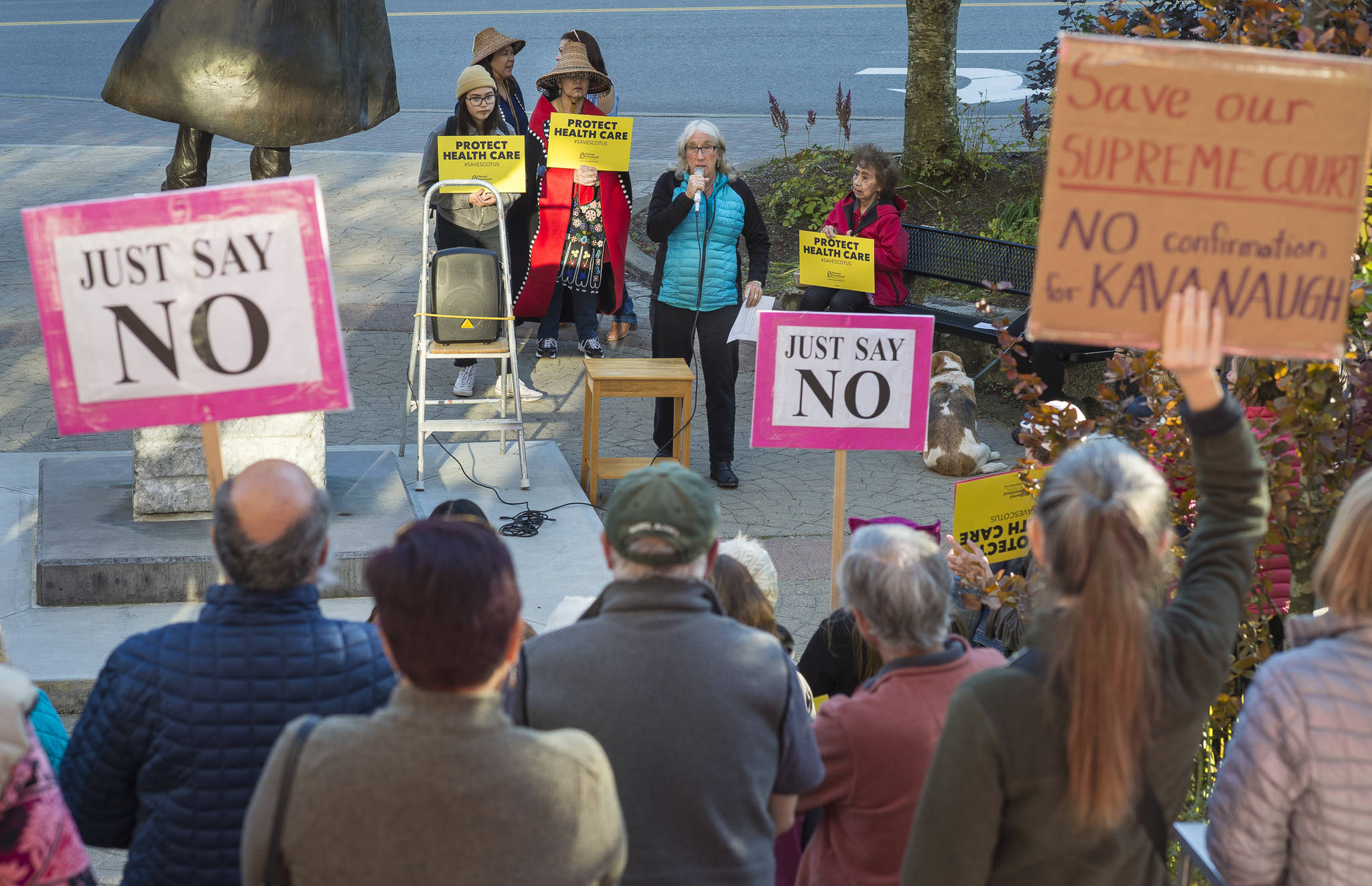 Juneau residents listen to Kate Troll as they participate in a protest against President Donald Trump’s nominee to the Supreme Court, Brett Kavanaugh, at Dimond Courthouse Plaza on Tuesday, Sept. 18, 2018. (Michael Penn | Juneau Empire)