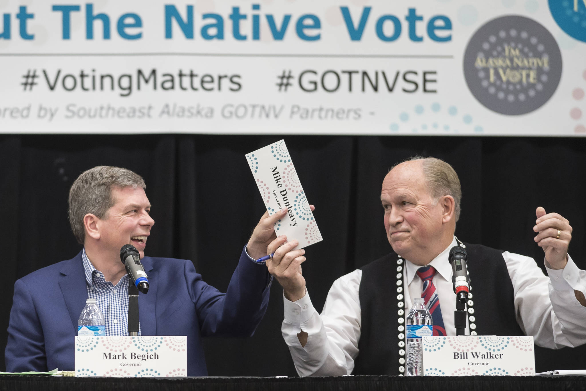 Former U.S. Sen. Mark Begich, left, and Gov. Bill Walker pass Mike Dunleavy’s name plate during a Special Native Issues Forum for governor candidates at the Elizabeth Peratrovich Hall on Tuesday, Oct. 2, 2018. Libertarian candidate Billy Toien, out of picture to the left, requested the name plate. Dunleavy did not attend the forum. (Michael Penn | Juneau Empire)
