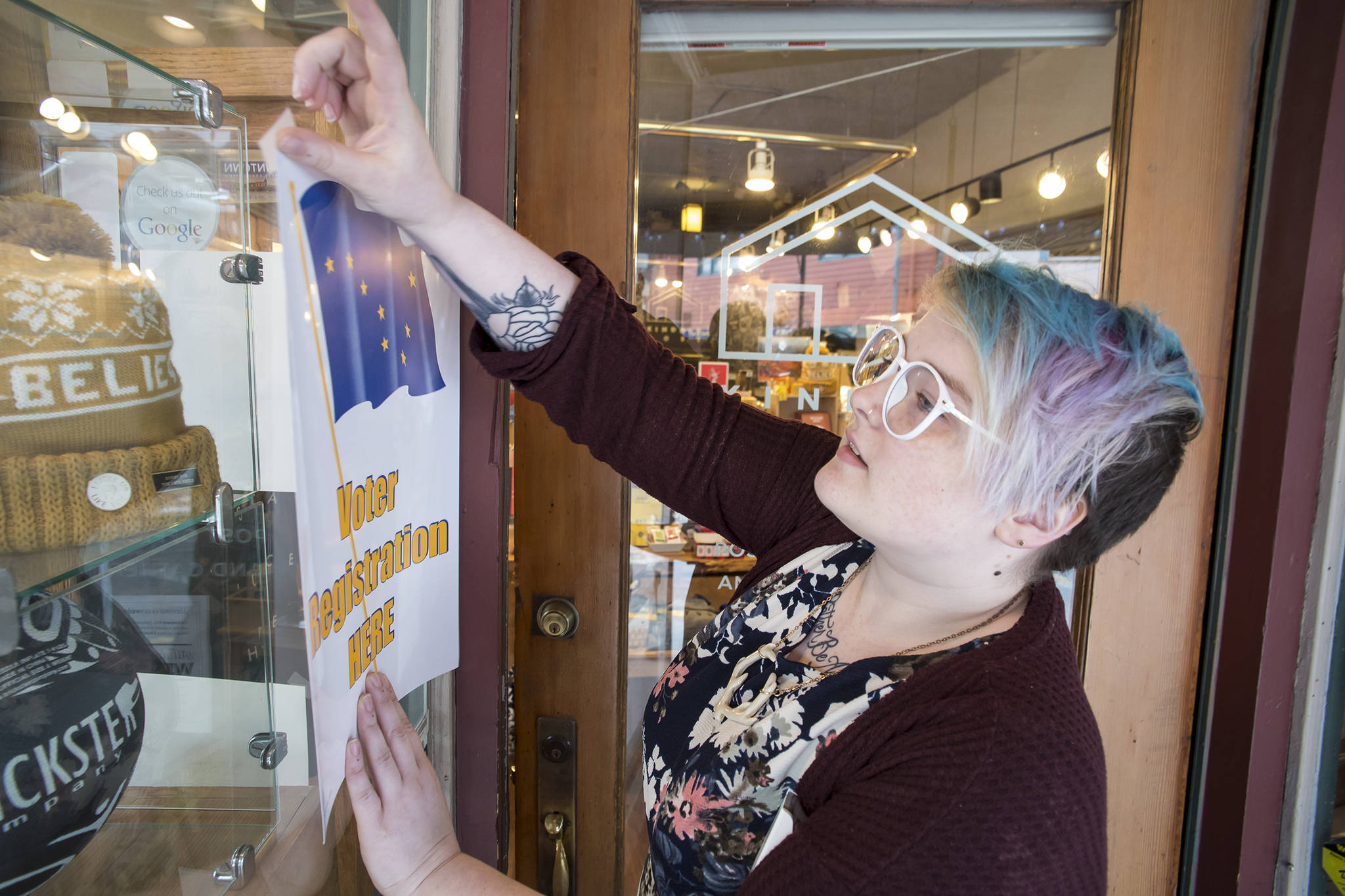 Veronica Buness, of Kindred Post, tapes up a sign on Thursday, Oct. 4, 2018, announcing people can register to vote at the Franklin Street business. (Michael Penn | Juneau Empire)