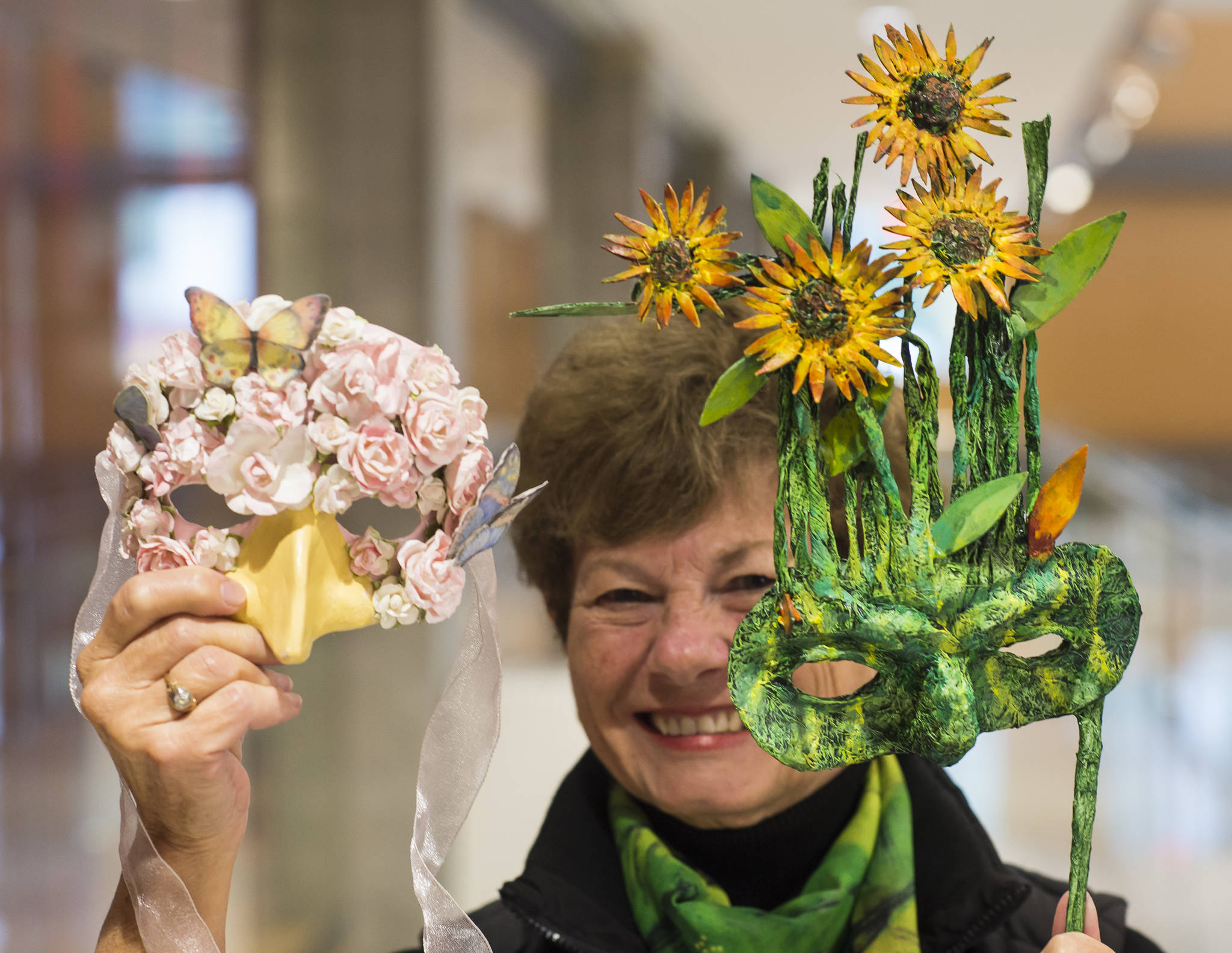 Mary Lou Gerbi, president of the Friends of the Alaska State Library, Archives, and Museum, holds two of the artist’s masks on Thursday, Oct. 11, 2018, that will be auctioned off during their MASK-erade event on Saturday, Oct. 20, 2018. (Michael Penn | Juneau Empire)
