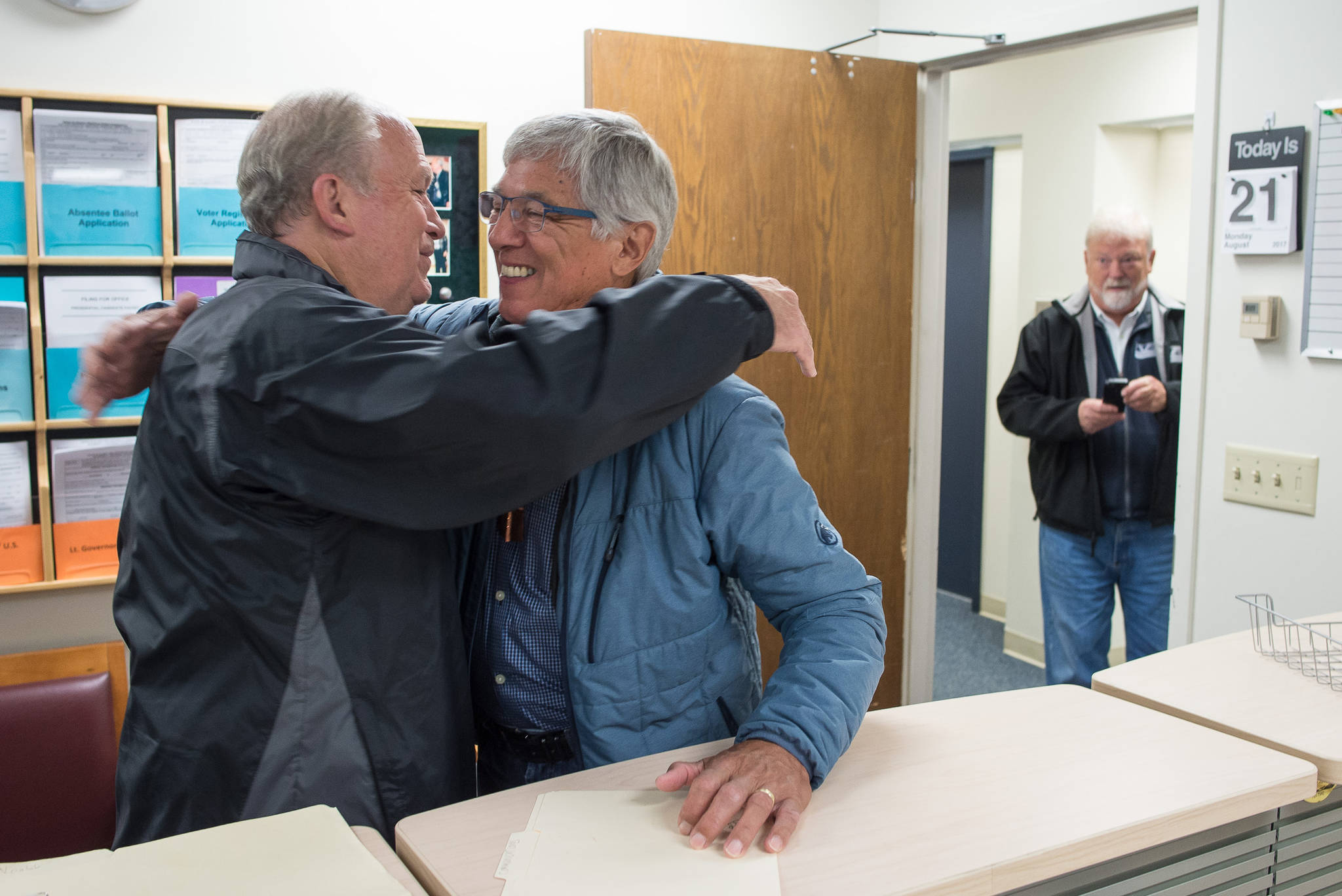 Gov. Bill Walker and Lt. Gov. Byron Mallott embrace after filing for re-election at the state’s election office in Juneau on Monday, Aug. 21, 2017. Former Juneau Mayor and state attorney general Bruce Botelho, right, watched the pair file.