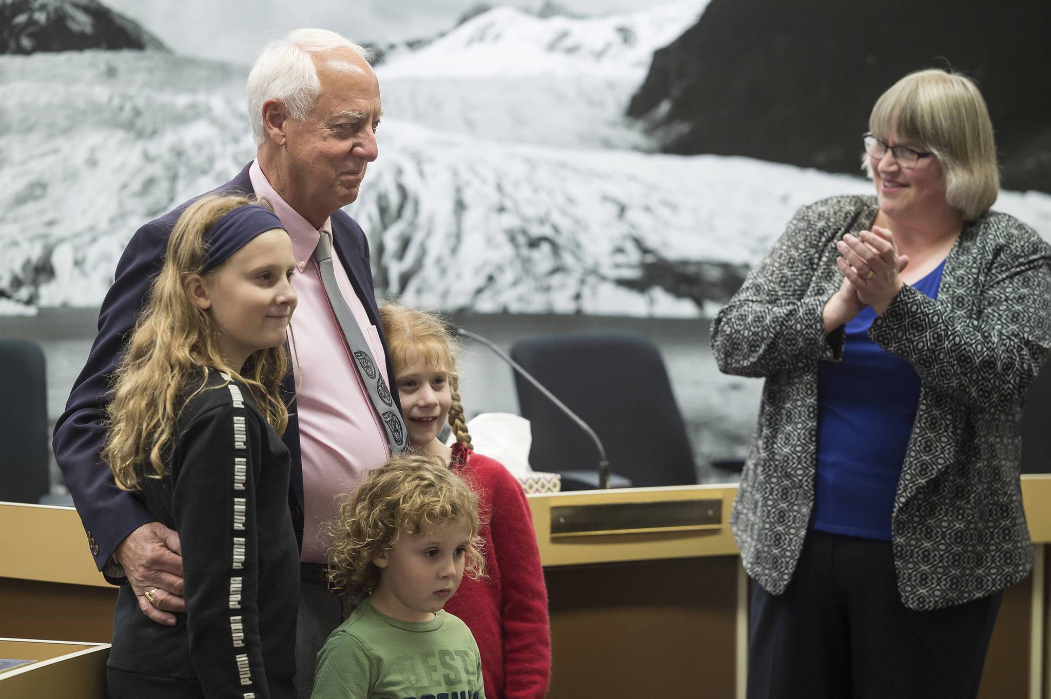 Outgoing Mayor Ken Koelsch, surrounded by his grandchildren, is acknowledged for his service by incoming Mayor Beth Weldon in a crowded Assembly chambers on Monday, Oct. 15, 2018. (Michael Penn | Juneau Empire)