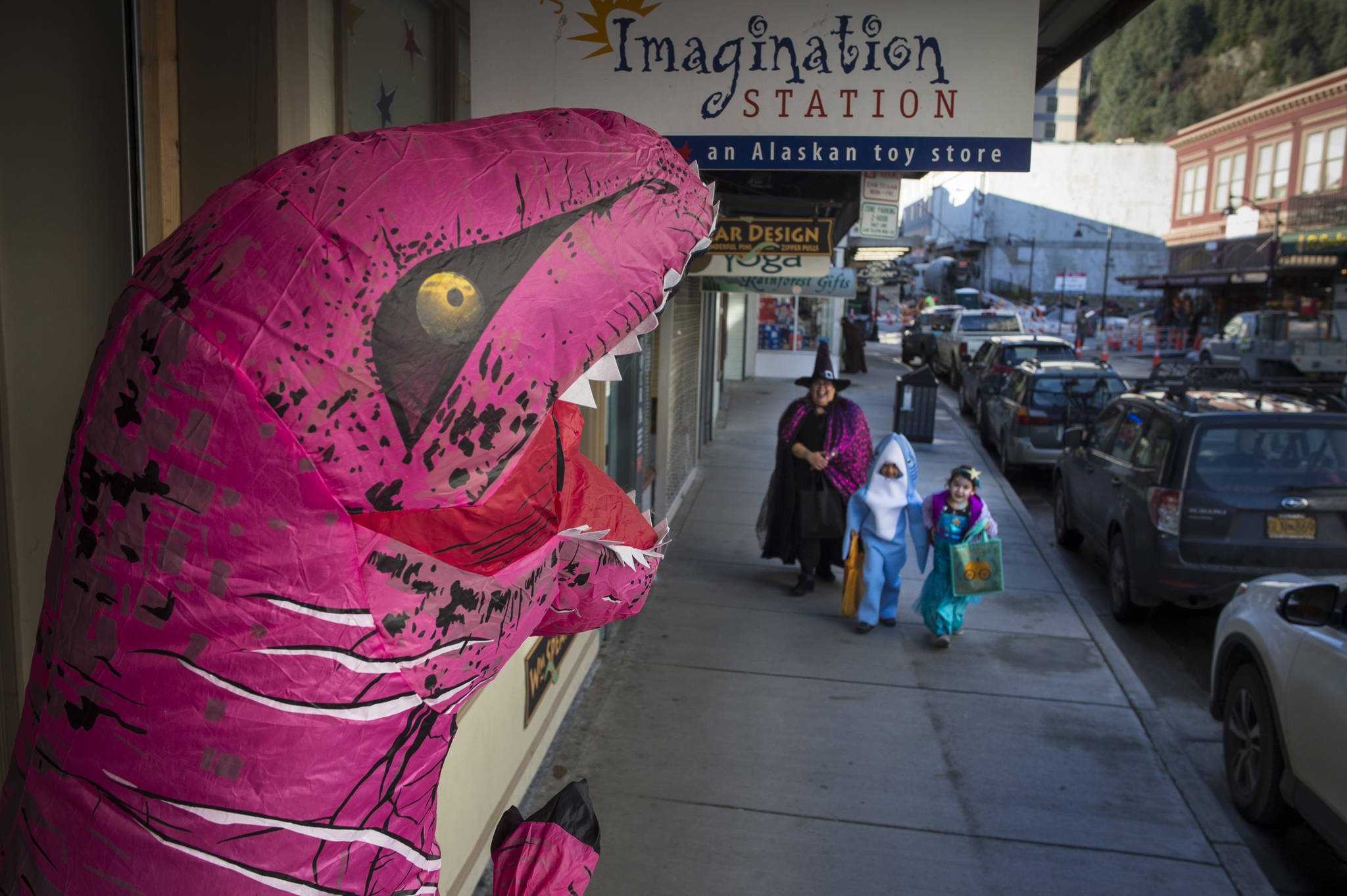 A T-Rex awaits Laura Cooper and her twins, Tanner and Amara, 5, in front of the Imagination Station on Wednesday, Oct. 31, 2018. For the fourth year Kindred Post has organized the Halloween celebration for trick-or-treaters. (Michael Penn | Juneau Empire)