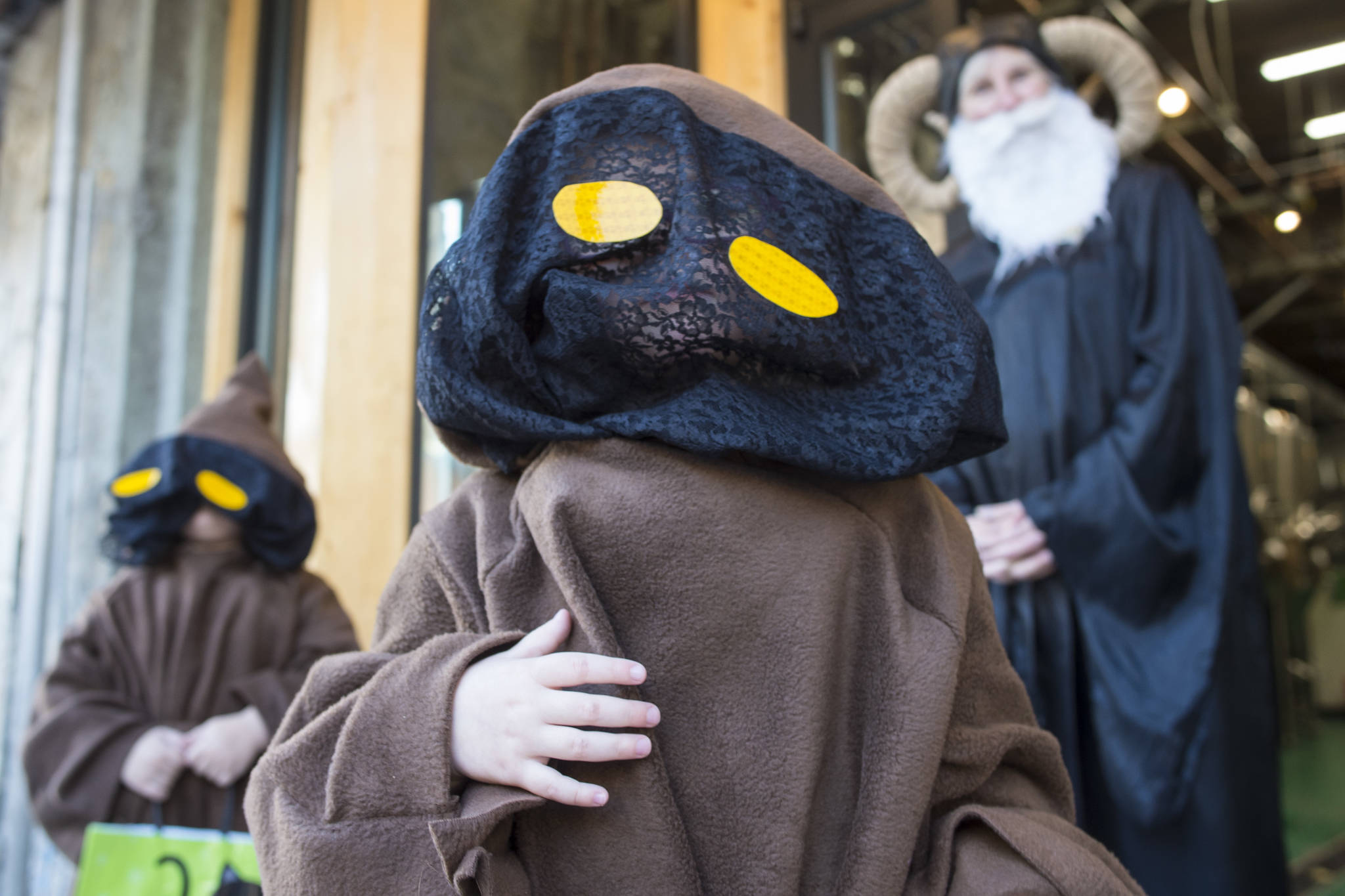 Aurelia Peoples, 4, center, and Mia Belvins, 3, are costumed as Jawas as they visit DJ Thomson at Devil’s Club Brewery on Wednesday, Oct. 31, 2018. For the fourth year Kindred Post has organized the Halloween celebration for trick-or-treaters. (Michael Penn | Juneau Empire)