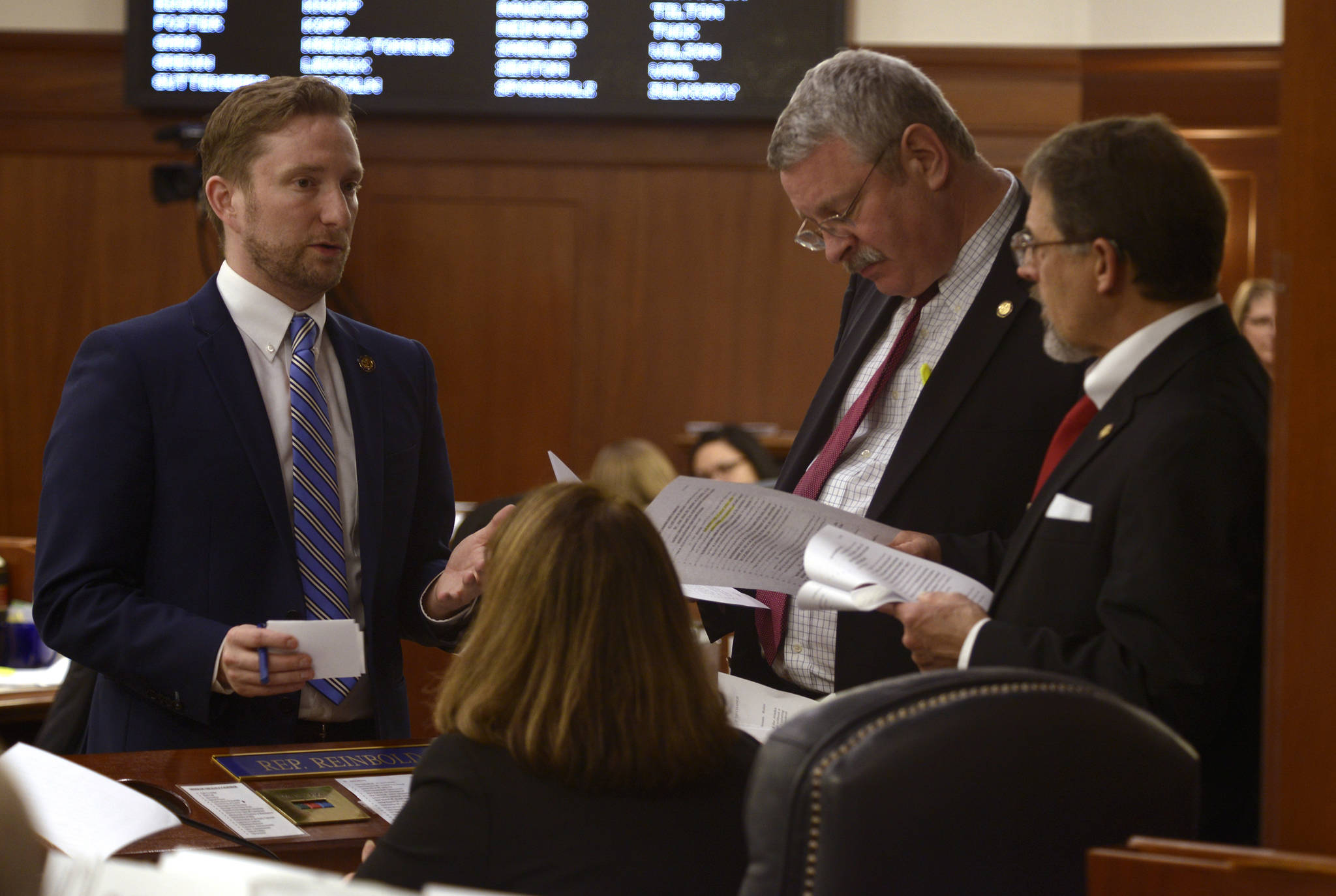 Rep. Jason Grenn, I-Anchorage (left) speaks to Rep. Dan Saddler, R-Eagle River (standing center), Rep. George Rauscher, R-Sutton (standing right) and Rep. Lora Reinbold, R-Eagle River (seated) before the final vote Friday, May 11, 2018 on House Bill 44. (Brian Hild | Alaska House Majority)