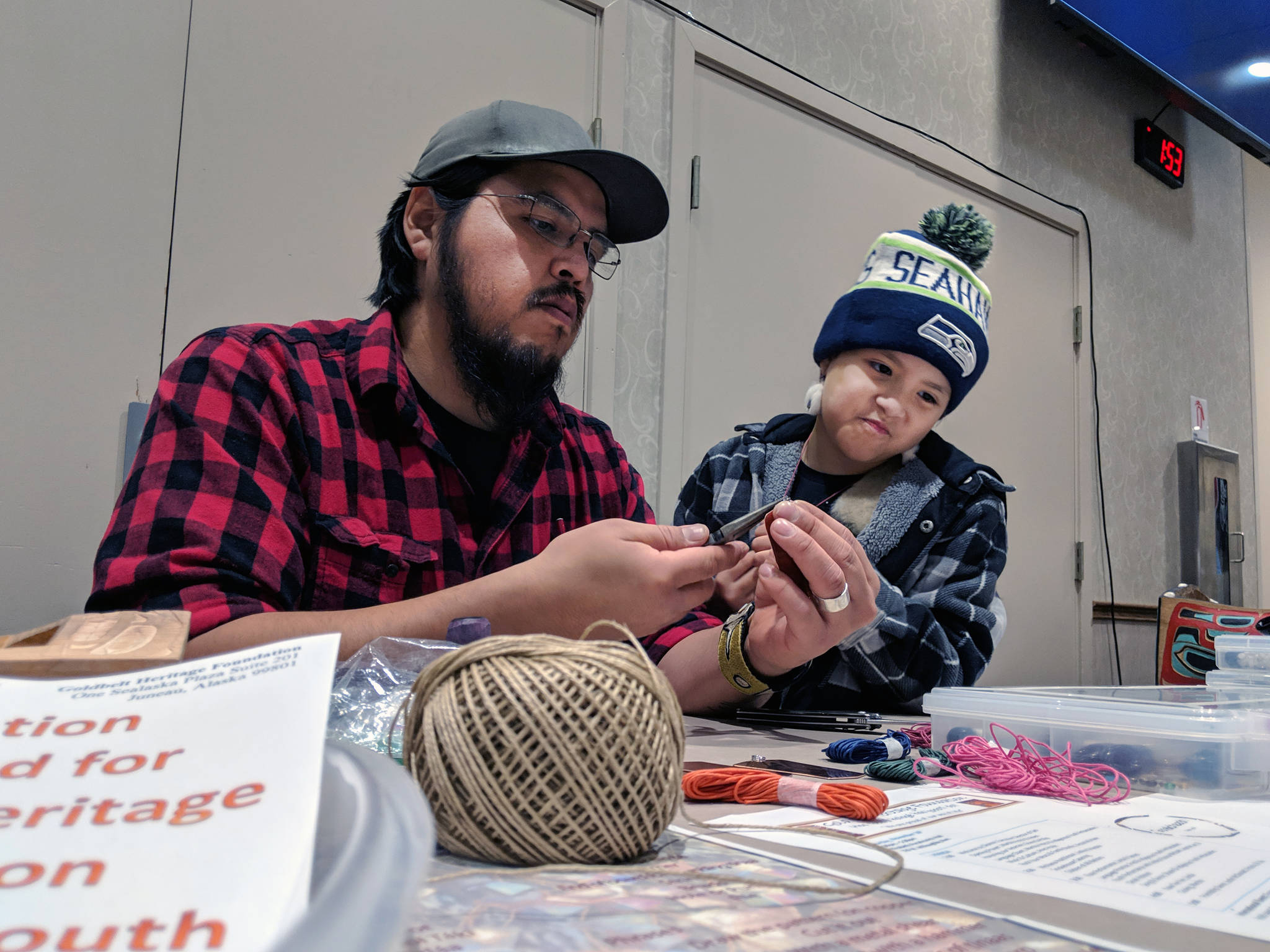 Herb(Kaaxtséen) Sheakley works on a tináa while Raven (Kátíx’di) Sheakley, 7, looks on during Rock Your Mocs, a celebration of Alaska Native Culture held Saturday. (Ben Hohenstatt | Capital City Weekly)