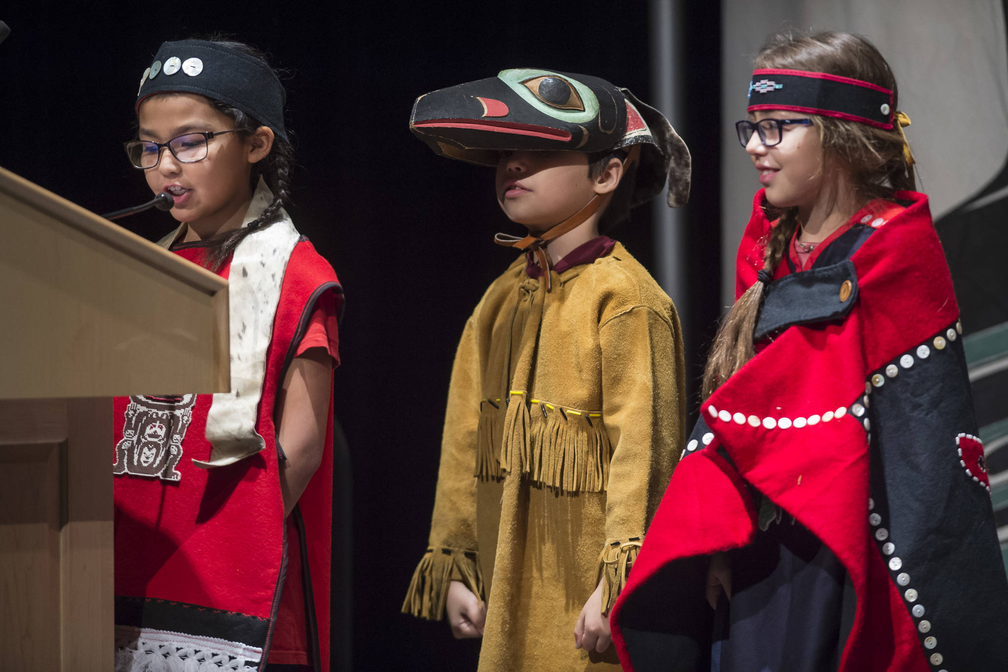 Torianna Johnson, left, Aiden Hood, center, and Marigold Lindoff of the Tlingit Culture Language and Literacy Dance Group from Harborview Elementary School address elders at the Voices of Our Ancestors Language Summit at Centennial Hall on Tuesday, Nov. 13, 2018. (Michael Penn | Juneau Empire)