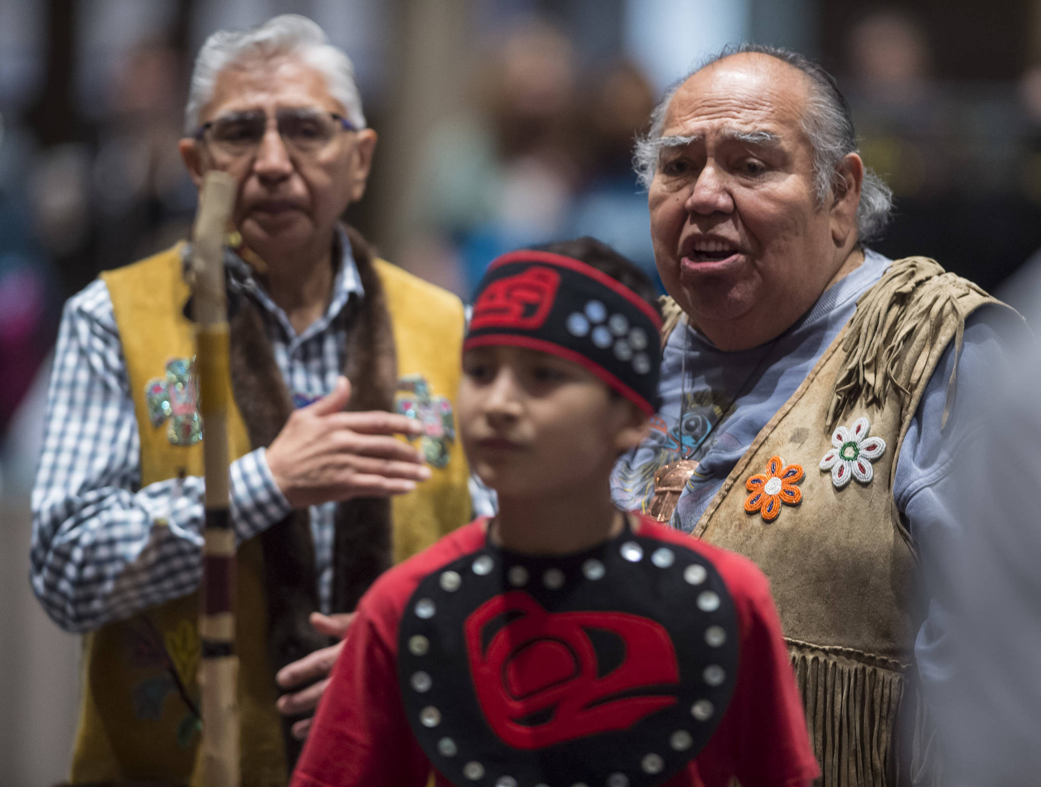 Tlingit elders David Katzeek, right, and Paul Marks, left, watch as Tyler Frisby, a member of the Tlingit Culture Language and Literacy Dance Group from Harborview Elementary School dance exits during the Voices of Our Ancestors Language Summit at Centennial Hall on Tuesday, Nov. 13, 2018. (Michael Penn | Juneau Empire)
