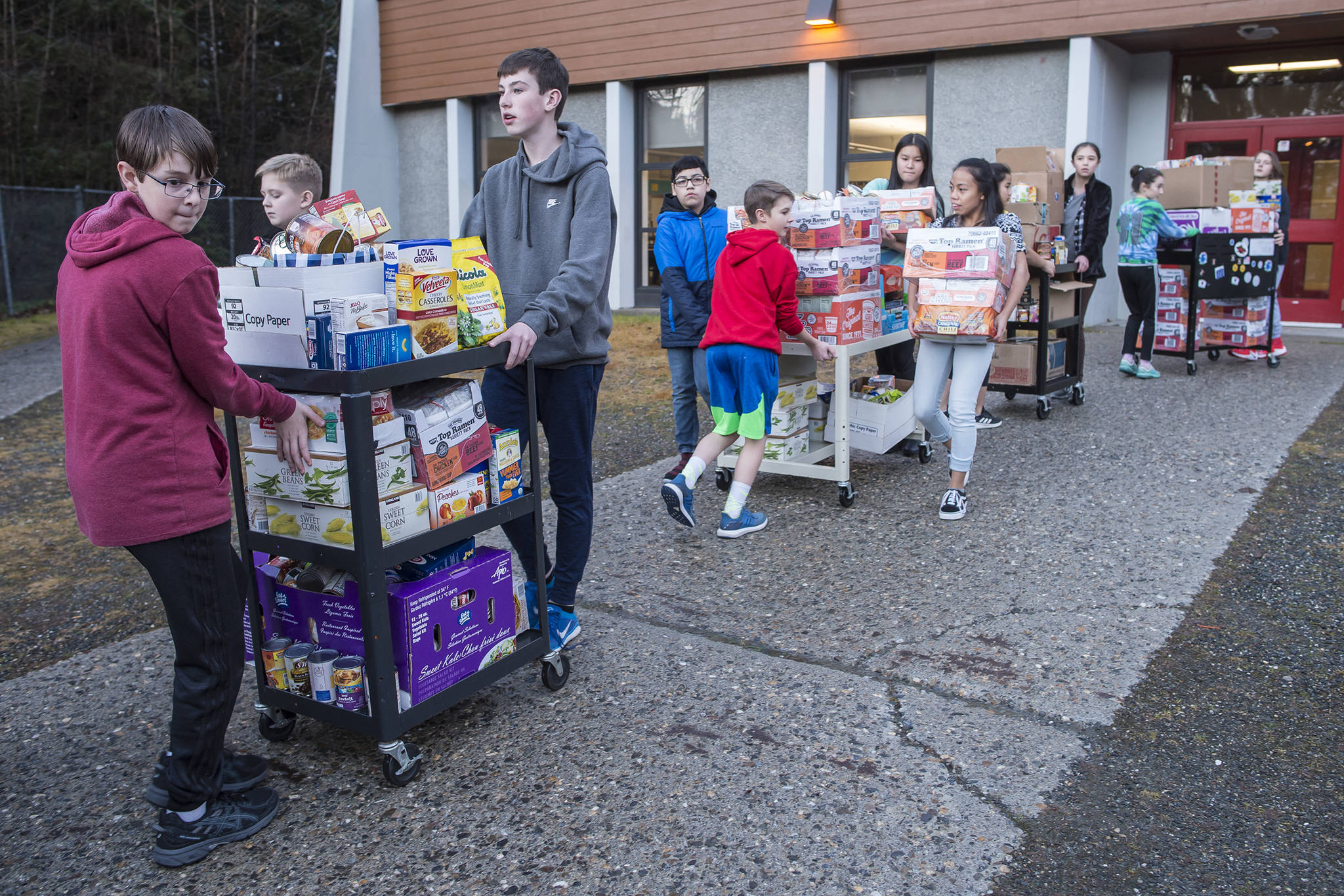 Lead by Student Body President eighth grader Grant Pierson, left, Floyd Dryden Middle School students uses carts to move donated food to a waiting Southeast Alaska Foodbank van on Tuesday, Nov. 20, 2018. (Michael Penn | Juneau Empire)