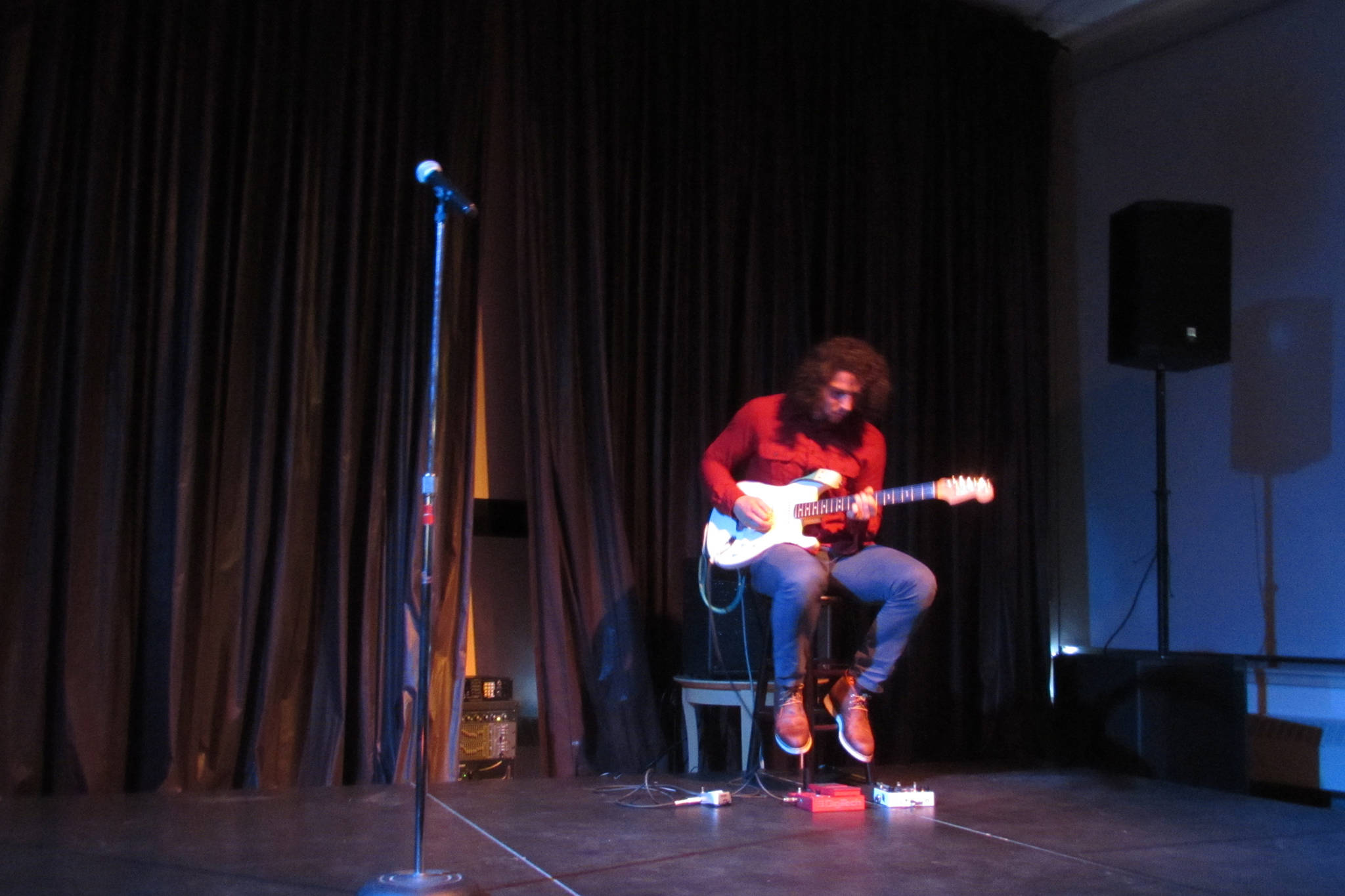 Avery Stewart on stage during the Woosh Kinaadeiyí Poetry Slam, Oct. 20. With the pedals near his feet, Stewart can provide backing instrumental loops for his guitar playing. (Ben Hohenstatt | Capital City Weekly)